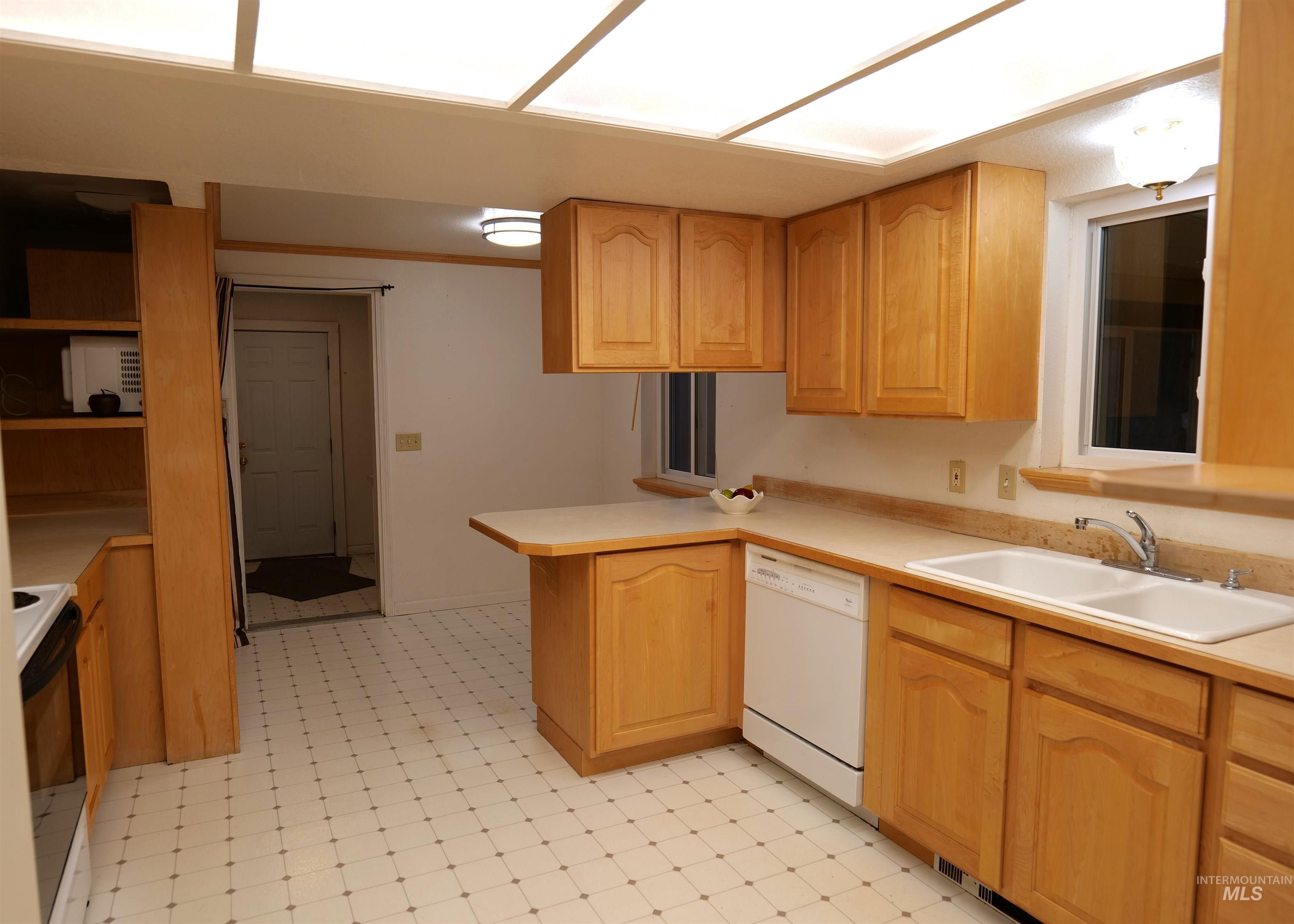 Kitchen featuring light wood cabinetry, laminate countertops, a double basin sink, and an integrated dishwasher