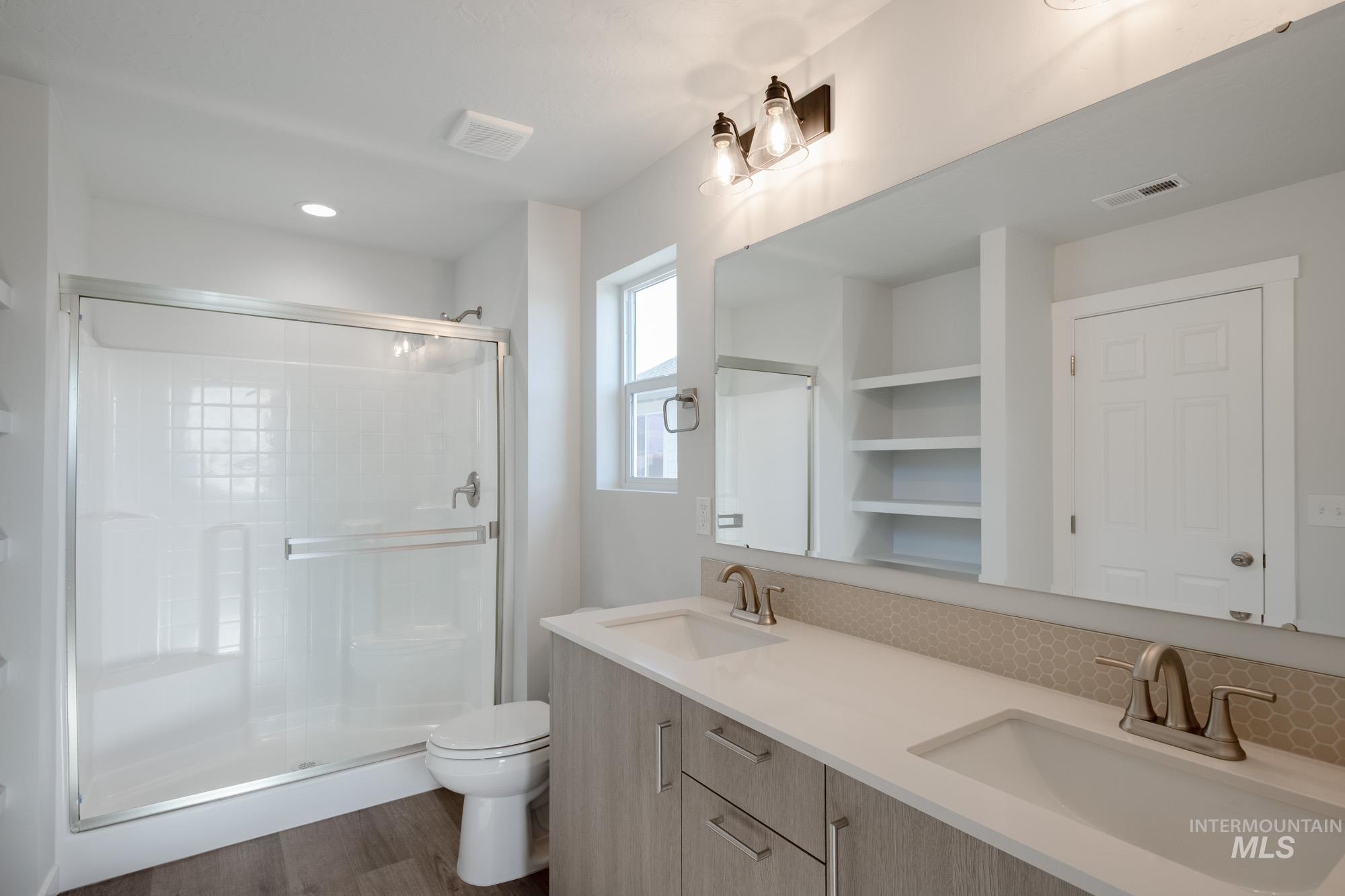 Full bath with double vanity, a shower stall, dark wood finished floors, and recessed lighting