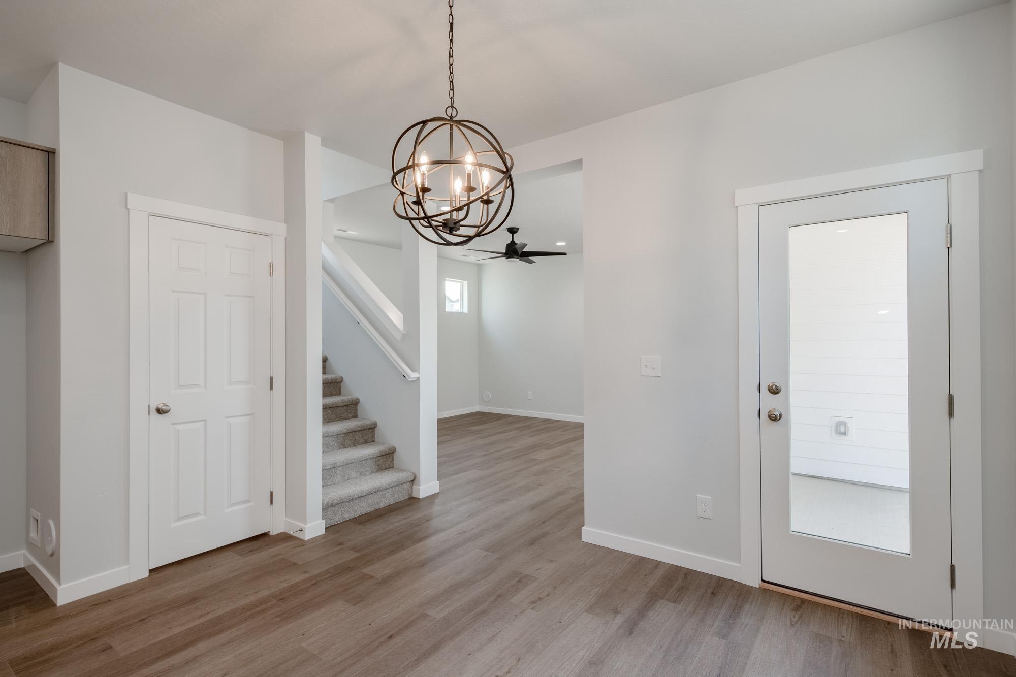 Unfurnished dining area featuring light wood-style flooring, stairs, a chandelier, and a ceiling fan