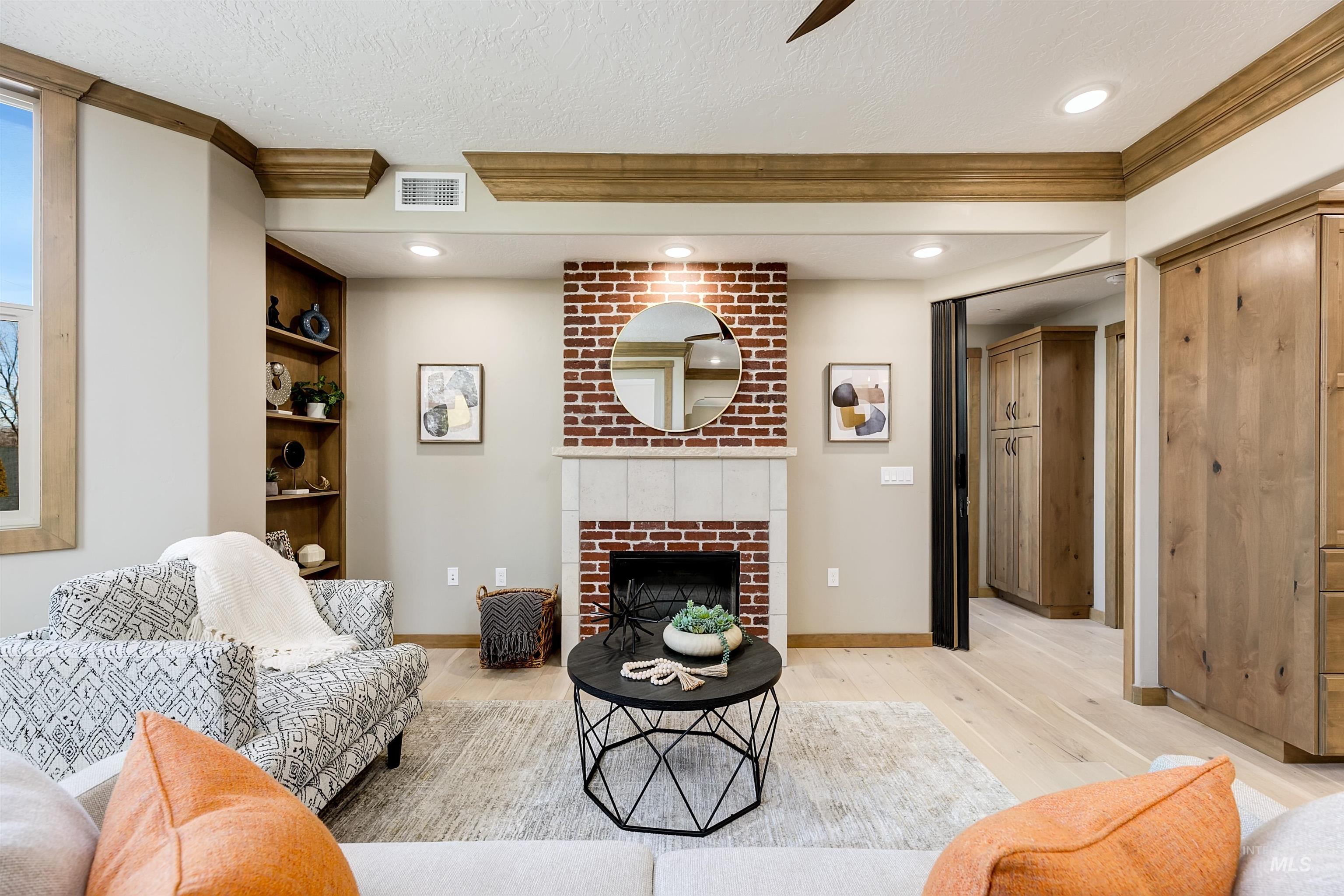 Living room featuring light wood-style flooring, a brick fireplace, ornamental molding, a textured ceiling, and recessed lighting