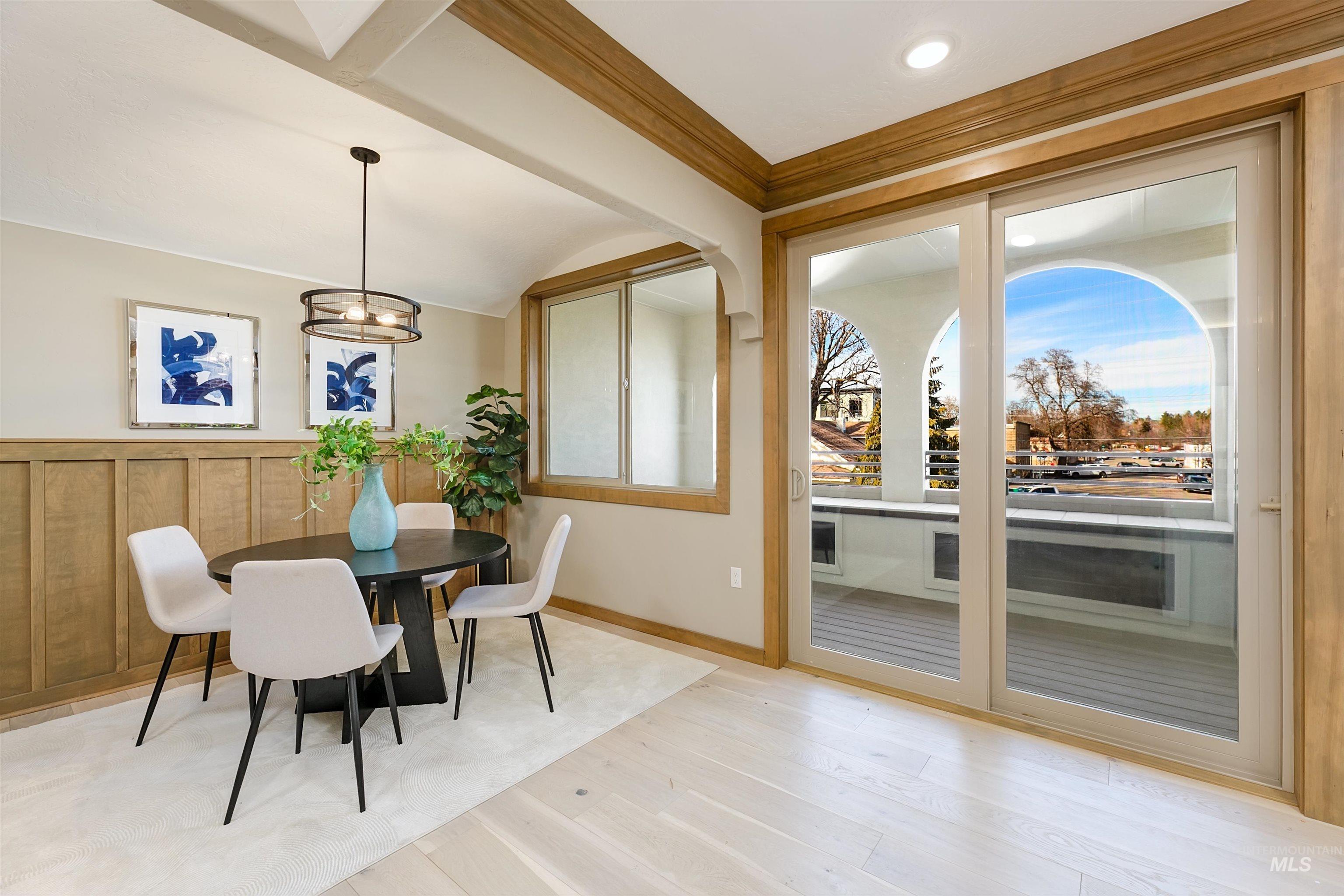 Dining area with light wood-type flooring, ornamental molding, vaulted ceiling, wainscoting, and a chandelier