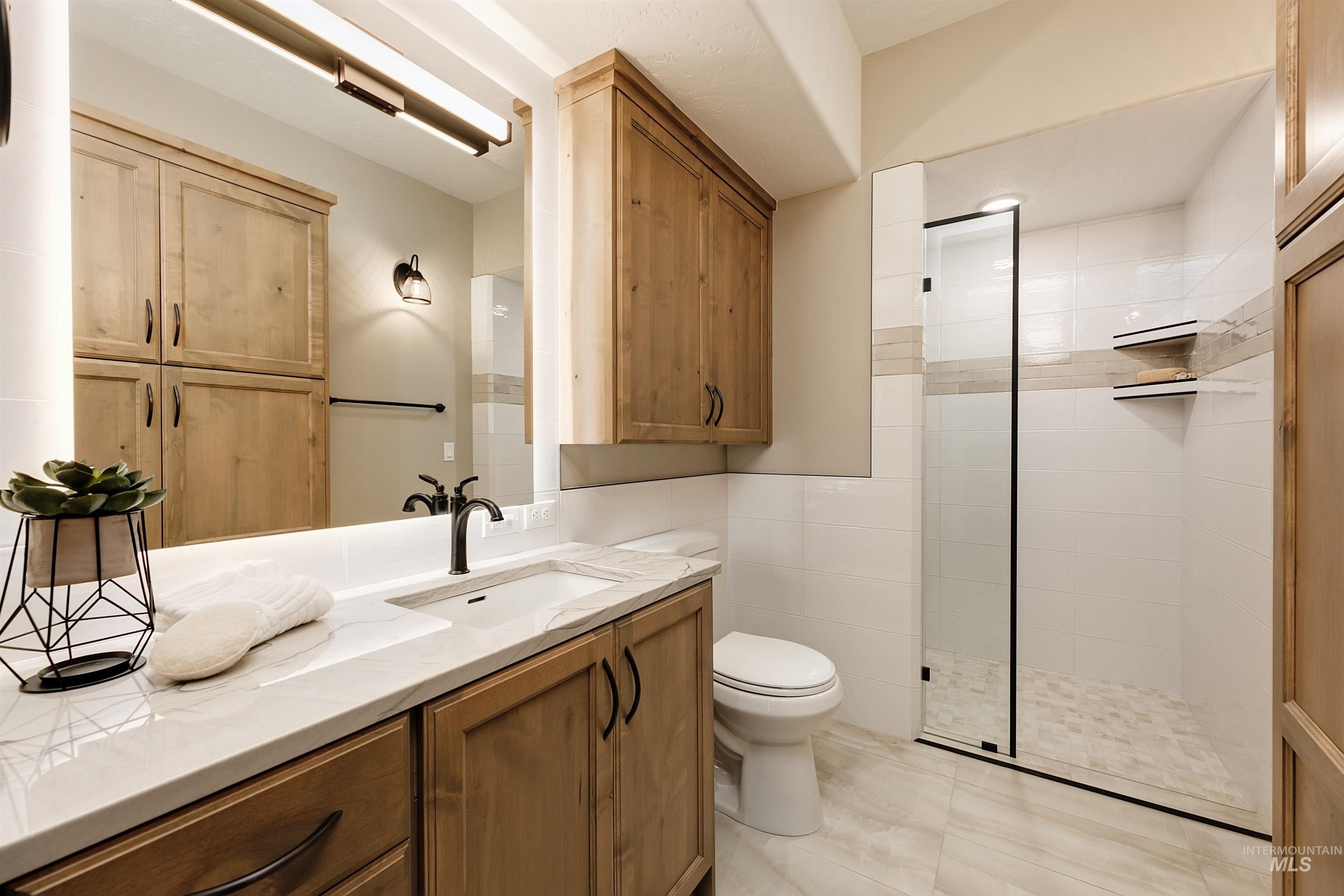 Full bath featuring vanity, a tile shower, and tile walls