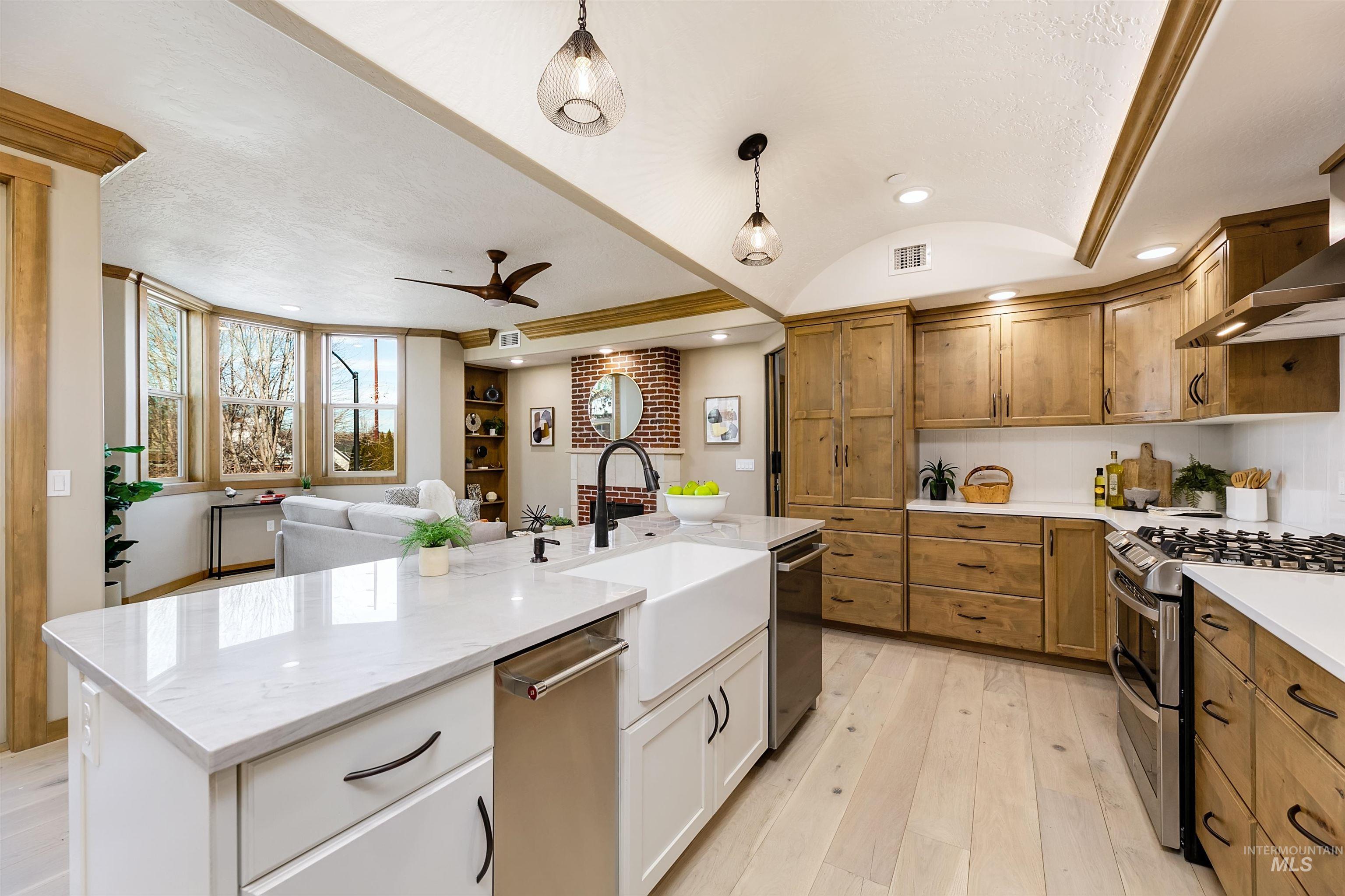 Kitchen with stainless steel appliances, light wood-style flooring, open floor plan, dual tone cabinets, and light stone countertops