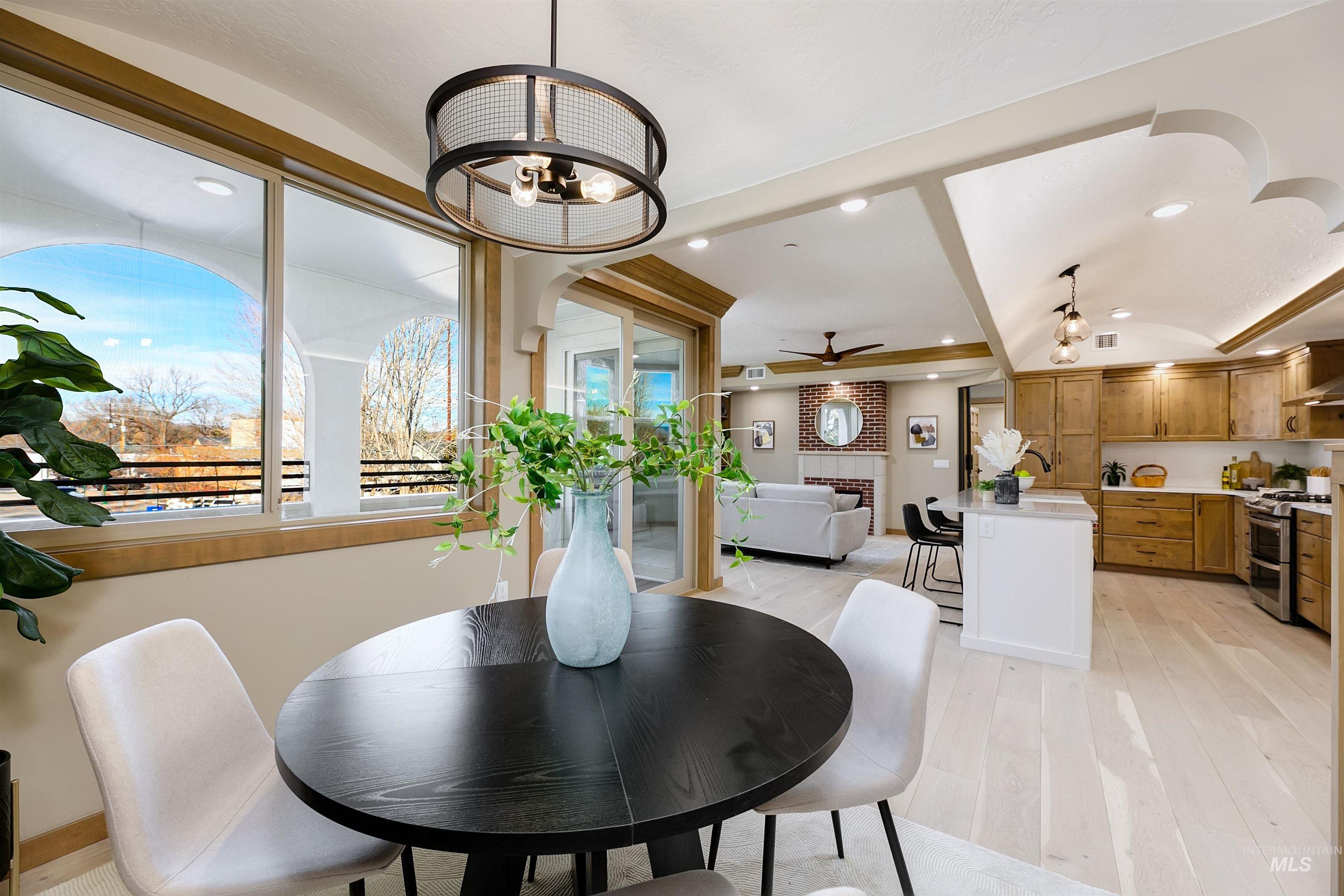 Dining space with a barrel ceiling, a brick fireplace, light wood finished floors, hanging lights, and a ceiling fan