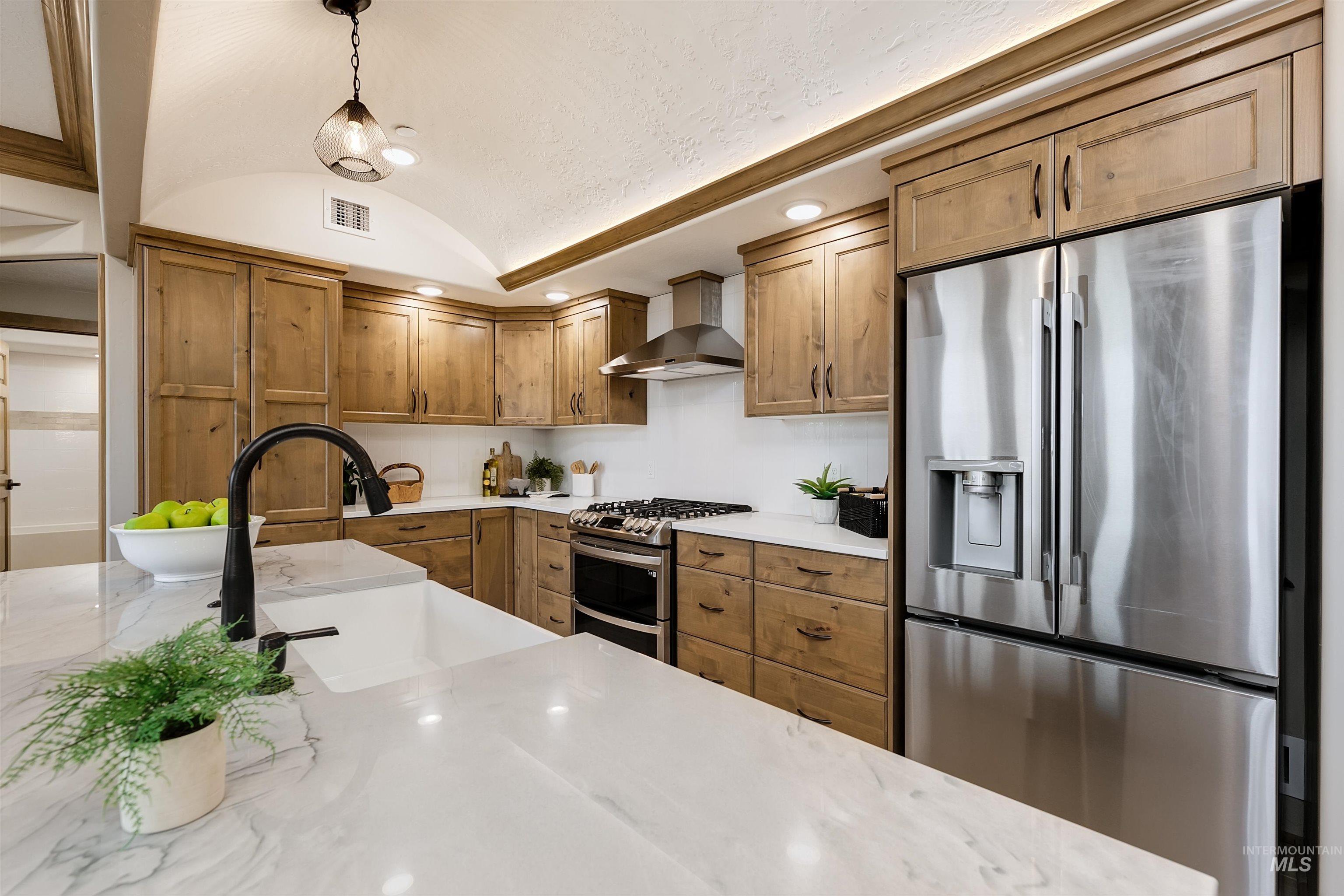 Kitchen featuring stainless steel appliances, wood finish cabinetry, pendant lighting, a barrel ceiling, and light stone countertops