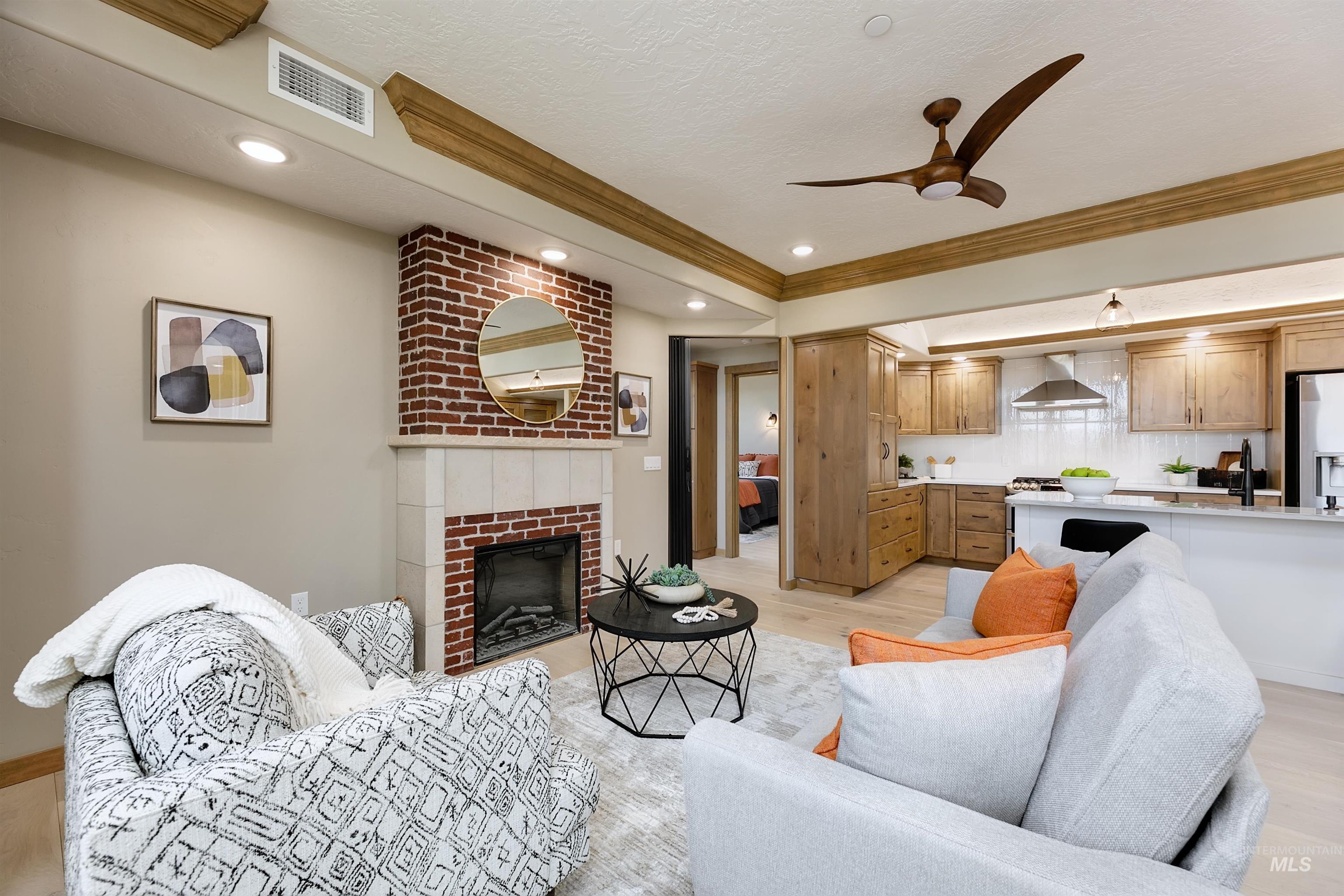 Living area featuring a brick fireplace, a ceiling fan, light wood finished floors, ornamental molding, and recessed lighting