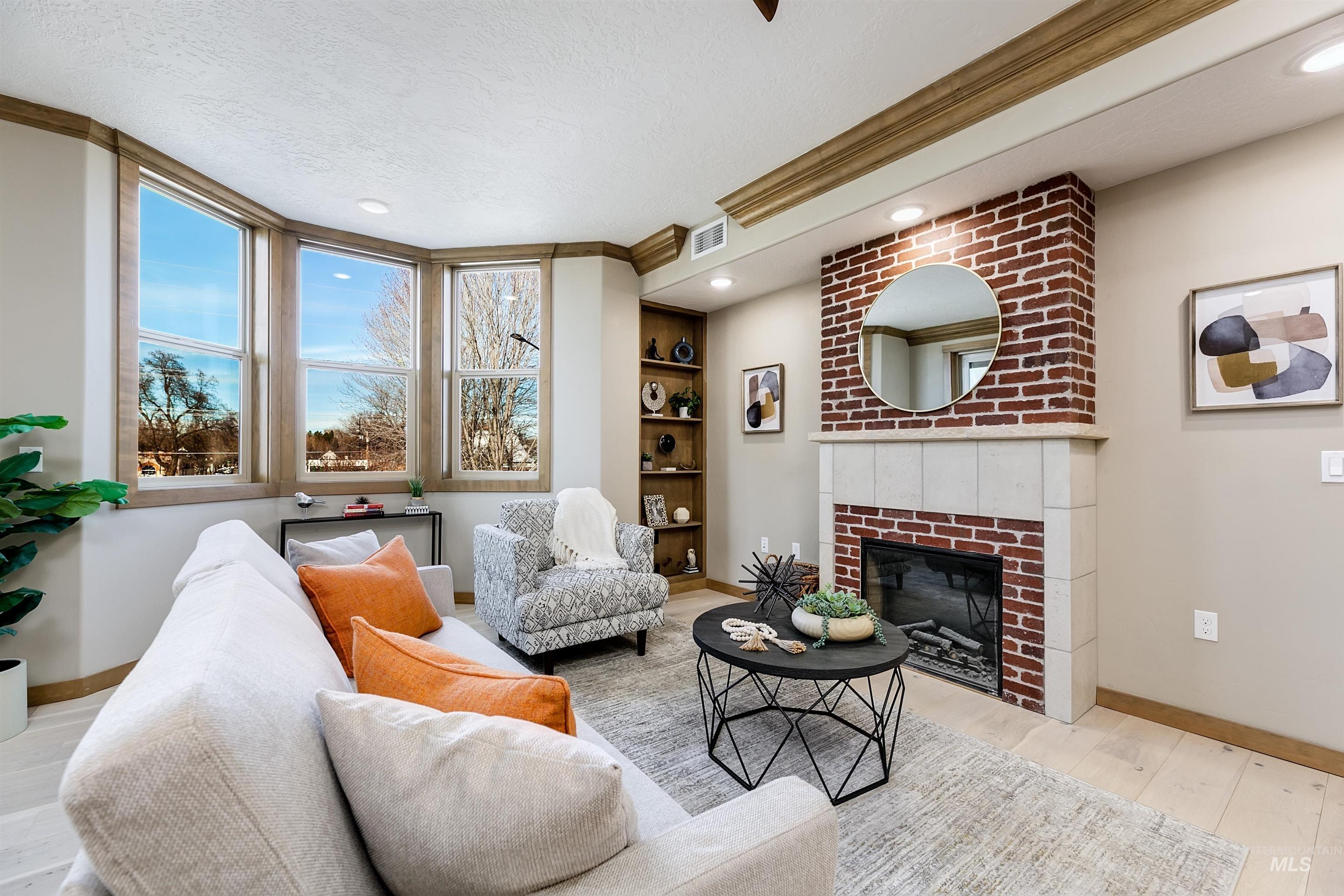 Living area featuring light wood-style floors, a brick fireplace, built in features, a textured ceiling, and recessed lighting