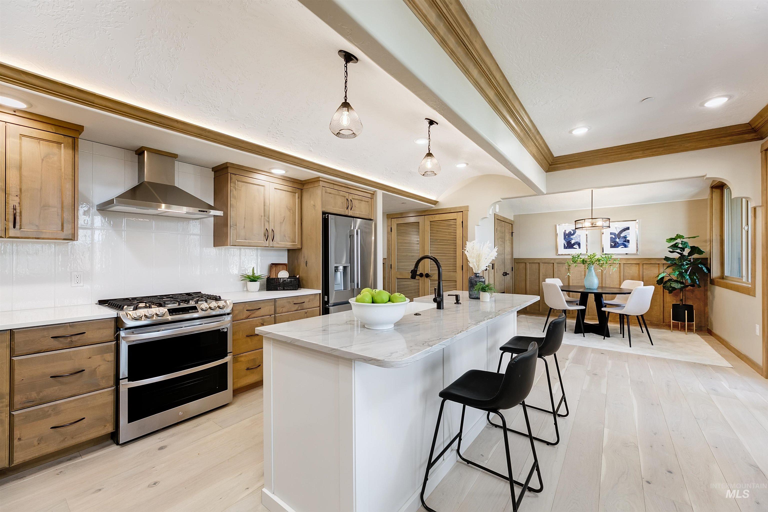 Kitchen with dual tone cabinetry, stainless steel appliances, light stone counters, decorative light fixtures, and light wood-type flooring