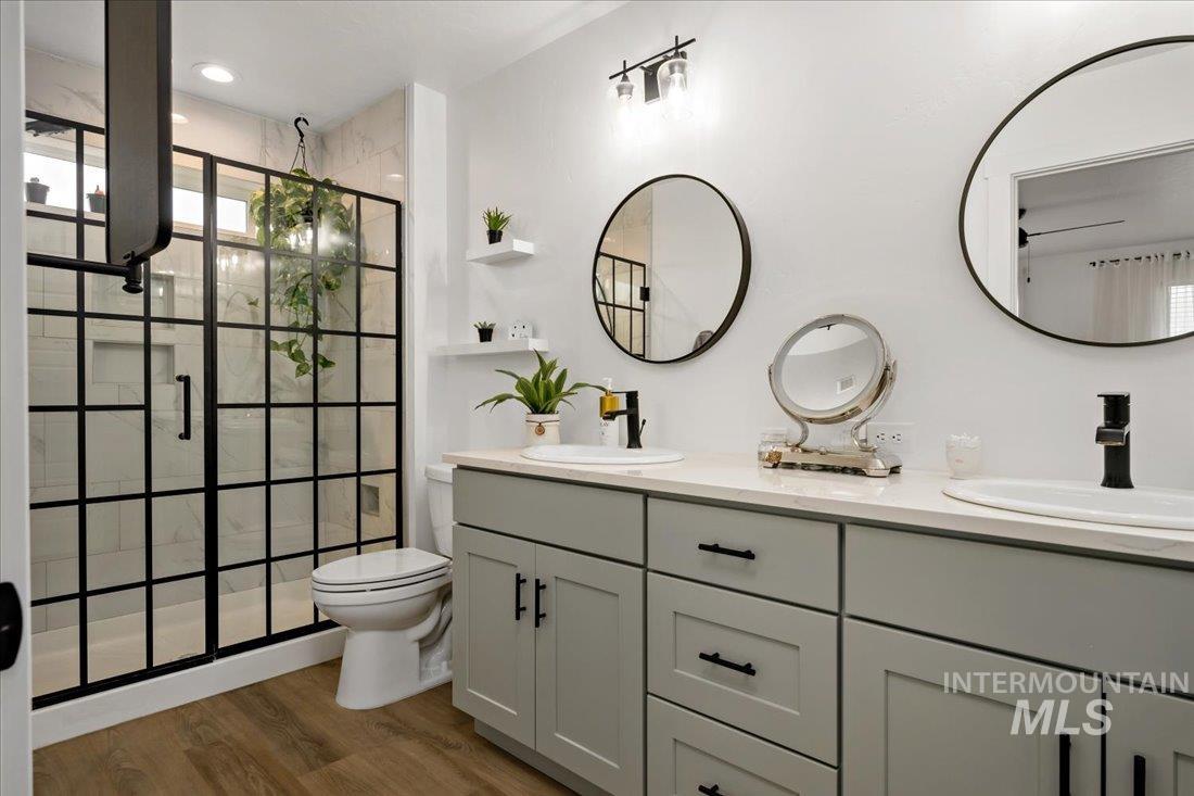 Full bathroom featuring a shower stall, double vanity, and wood finished floors