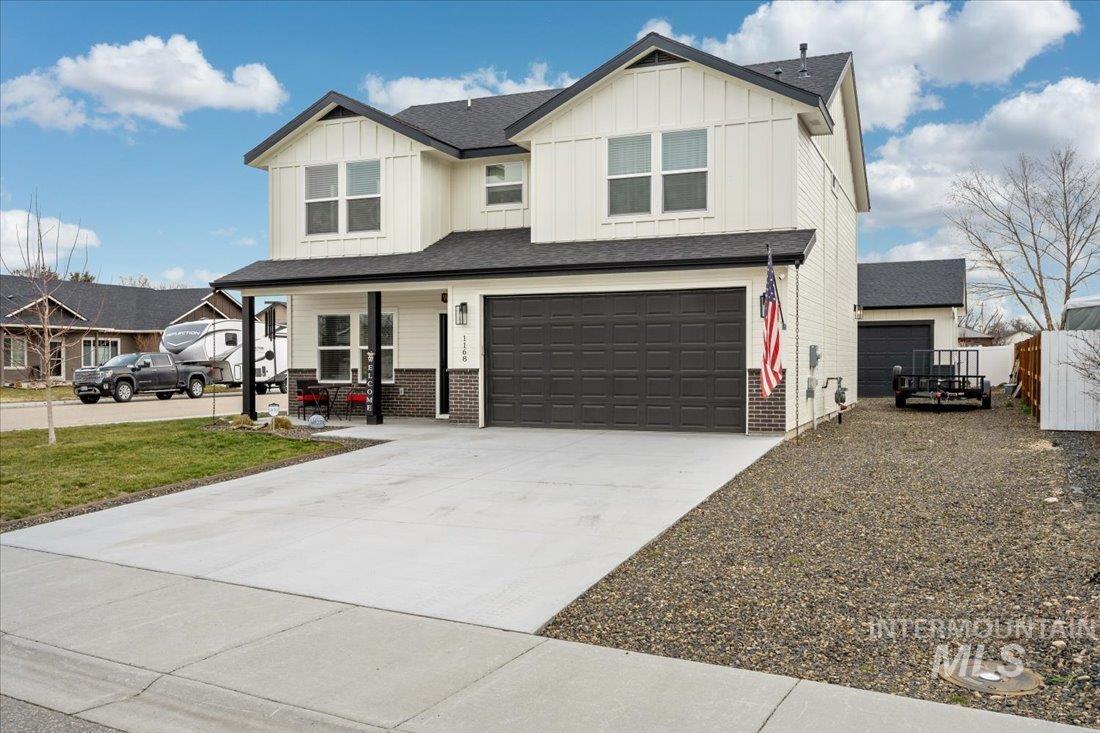 View of front of house featuring board and batten siding, a porch, driveway, an attached garage, and brick siding