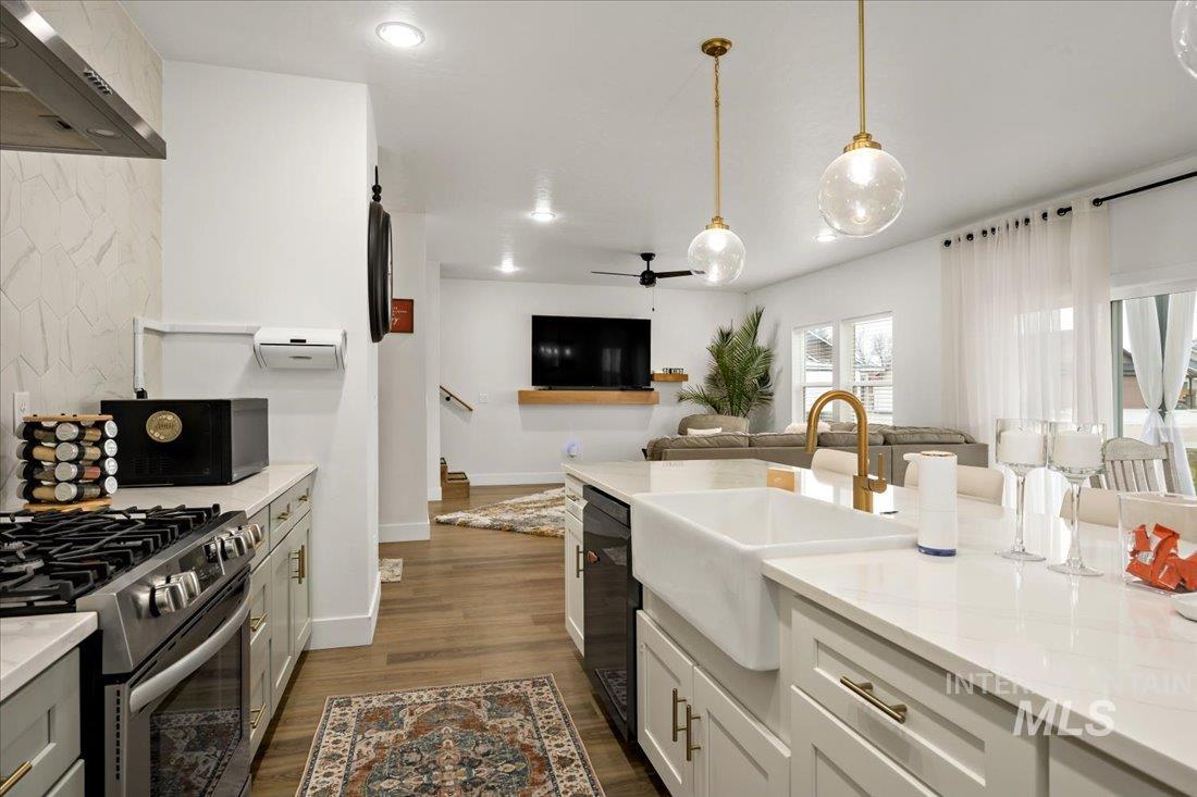 Kitchen with wall chimney range hood, open floor plan, dark wood-style floors, a ceiling fan, and decorative light fixtures