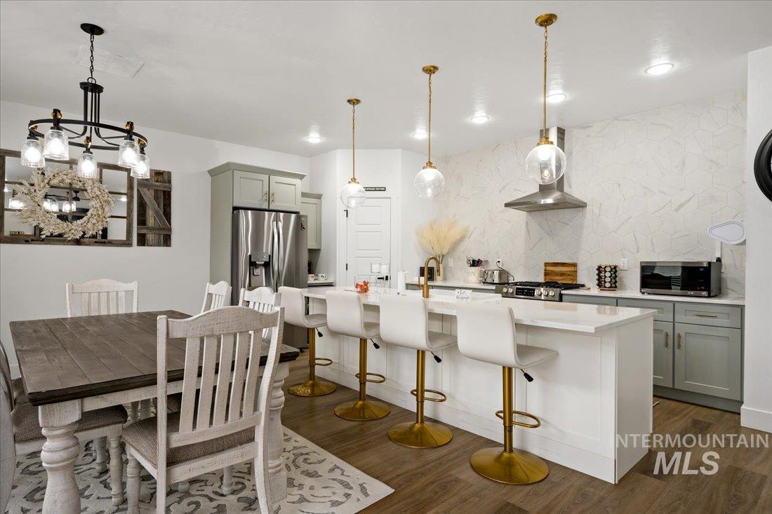 Kitchen featuring a kitchen bar, gray cabinetry, backsplash, an island with sink, and dark wood finished floors