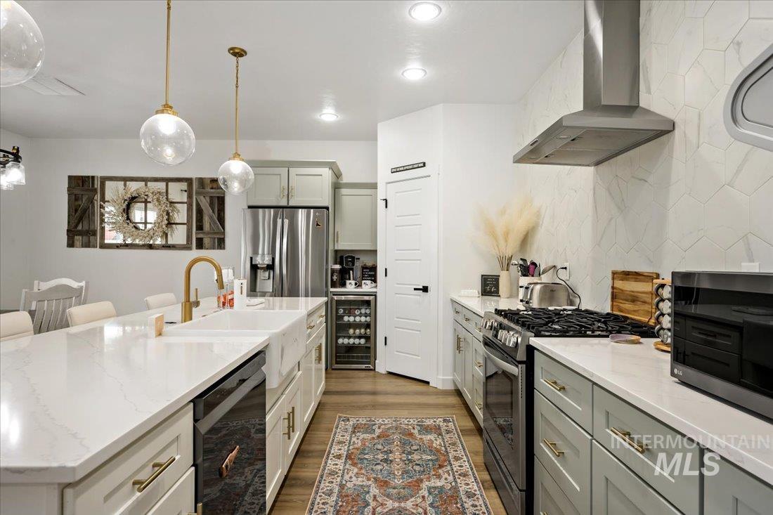 Kitchen featuring appliances with stainless steel finishes, wall chimney exhaust hood, dark wood-style floors, decorative light fixtures, and light stone countertops