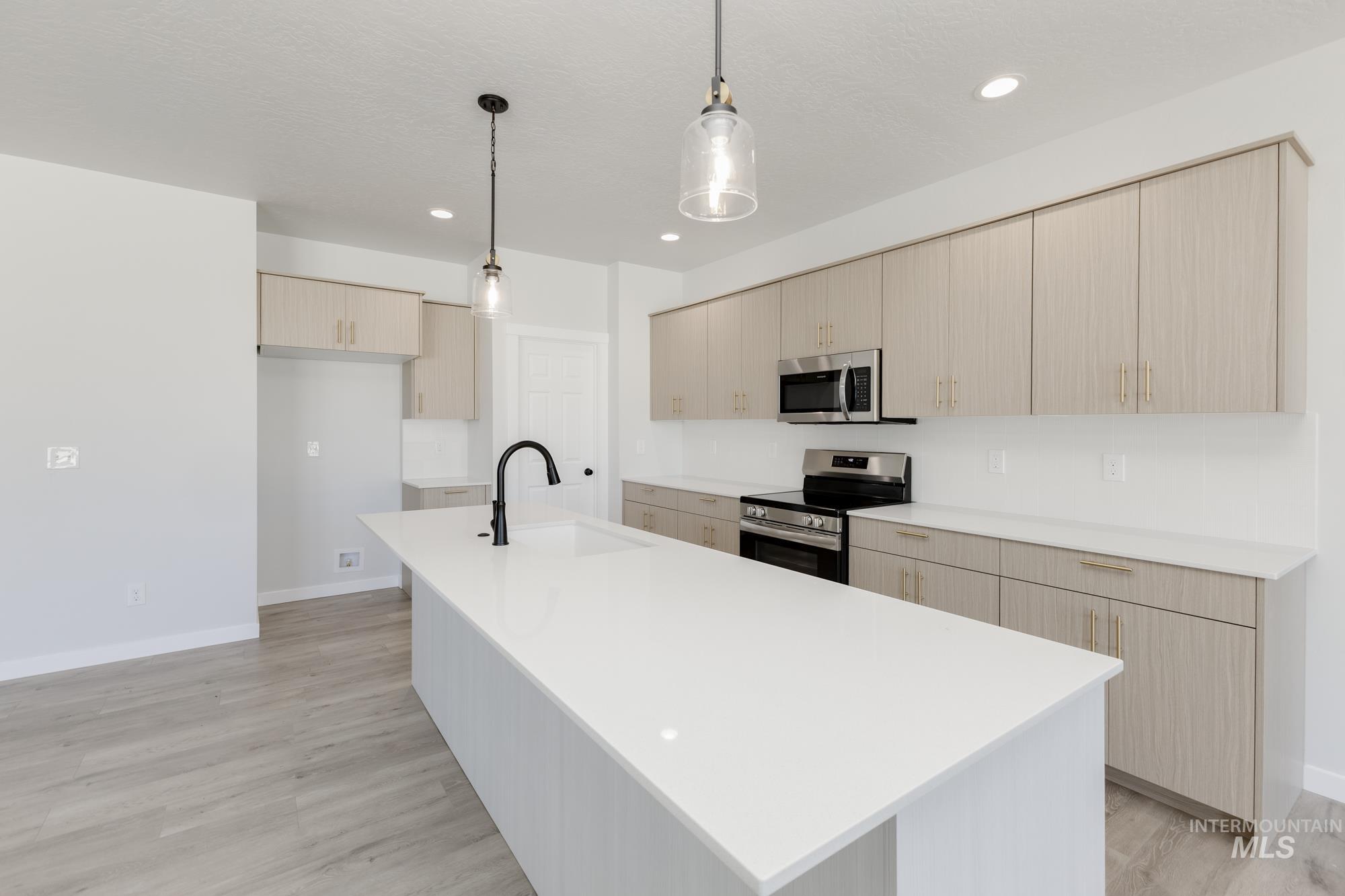 Kitchen featuring appliances with stainless steel finishes, decorative light fixtures, light brown cabinetry, light wood-style flooring, and modern cabinets