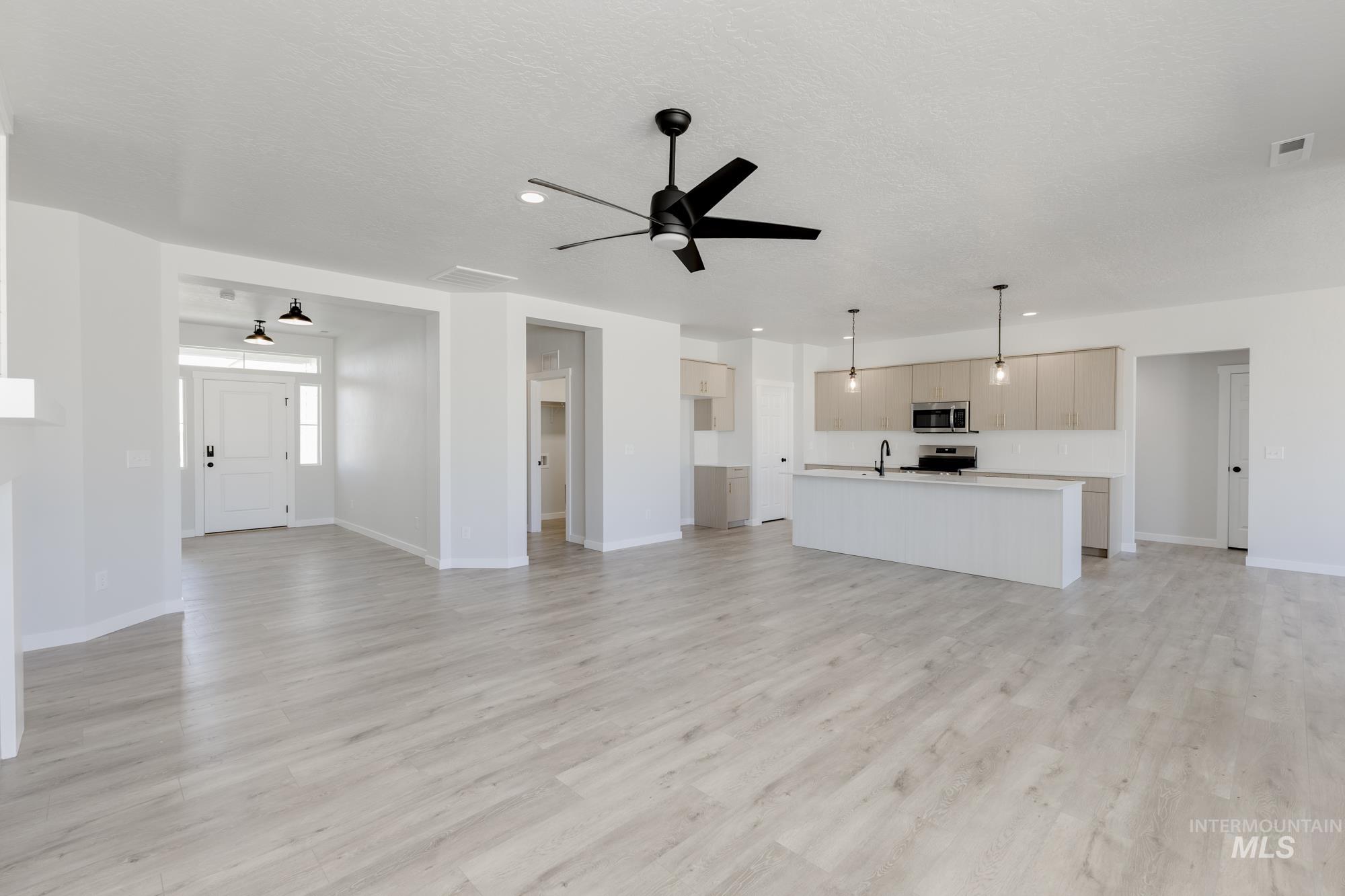 Unfurnished living room featuring a ceiling fan, light wood finished floors, and a textured ceiling