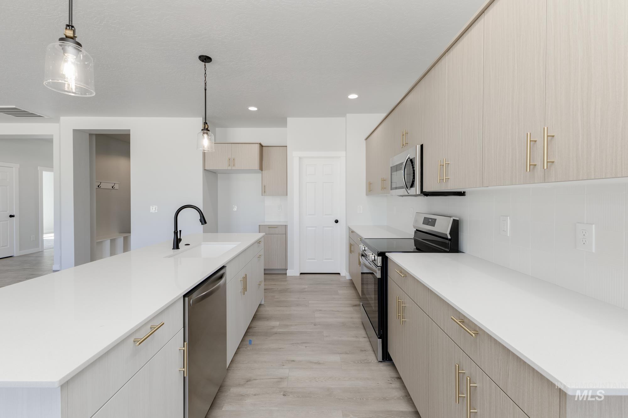 Kitchen with stainless steel appliances, pendant lighting, light wood-style floors, an island with sink, and recessed lighting