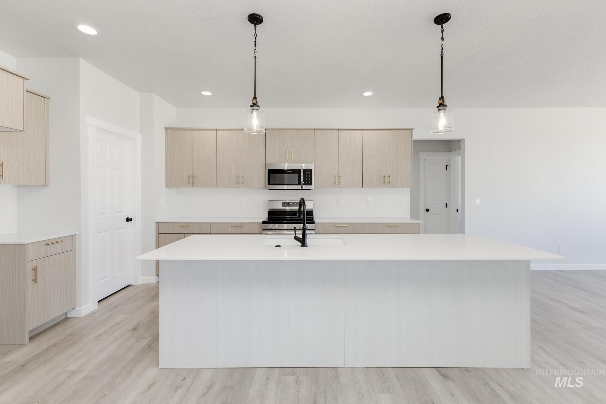 Kitchen with light brown cabinets, stainless steel appliances, light wood finished floors, pendant lighting, and recessed lighting