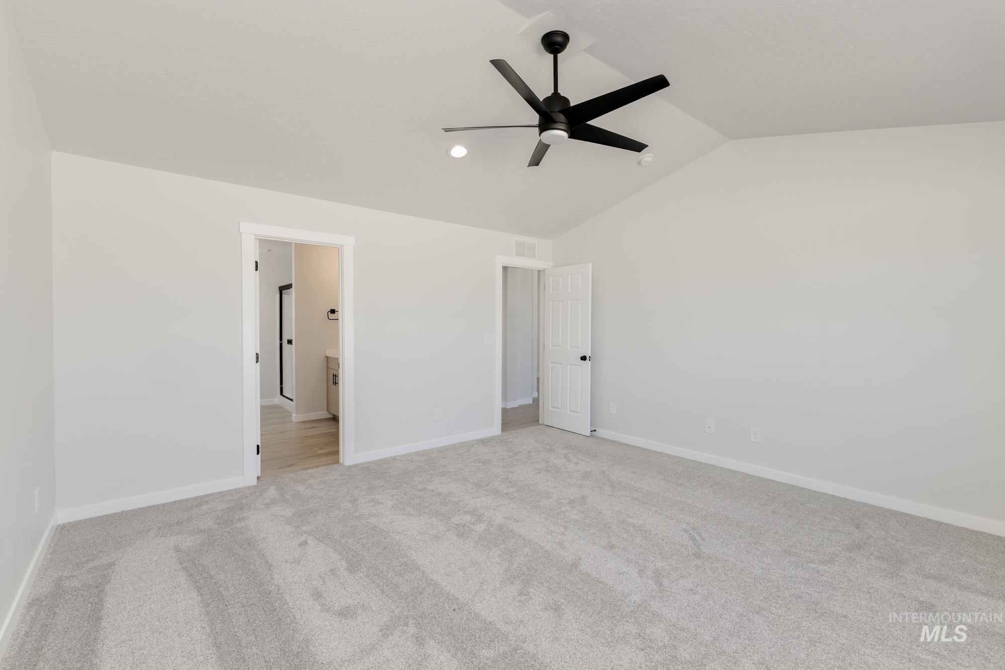 Unfurnished bedroom featuring lofted ceiling, light colored carpet, a ceiling fan, and ensuite bathroom