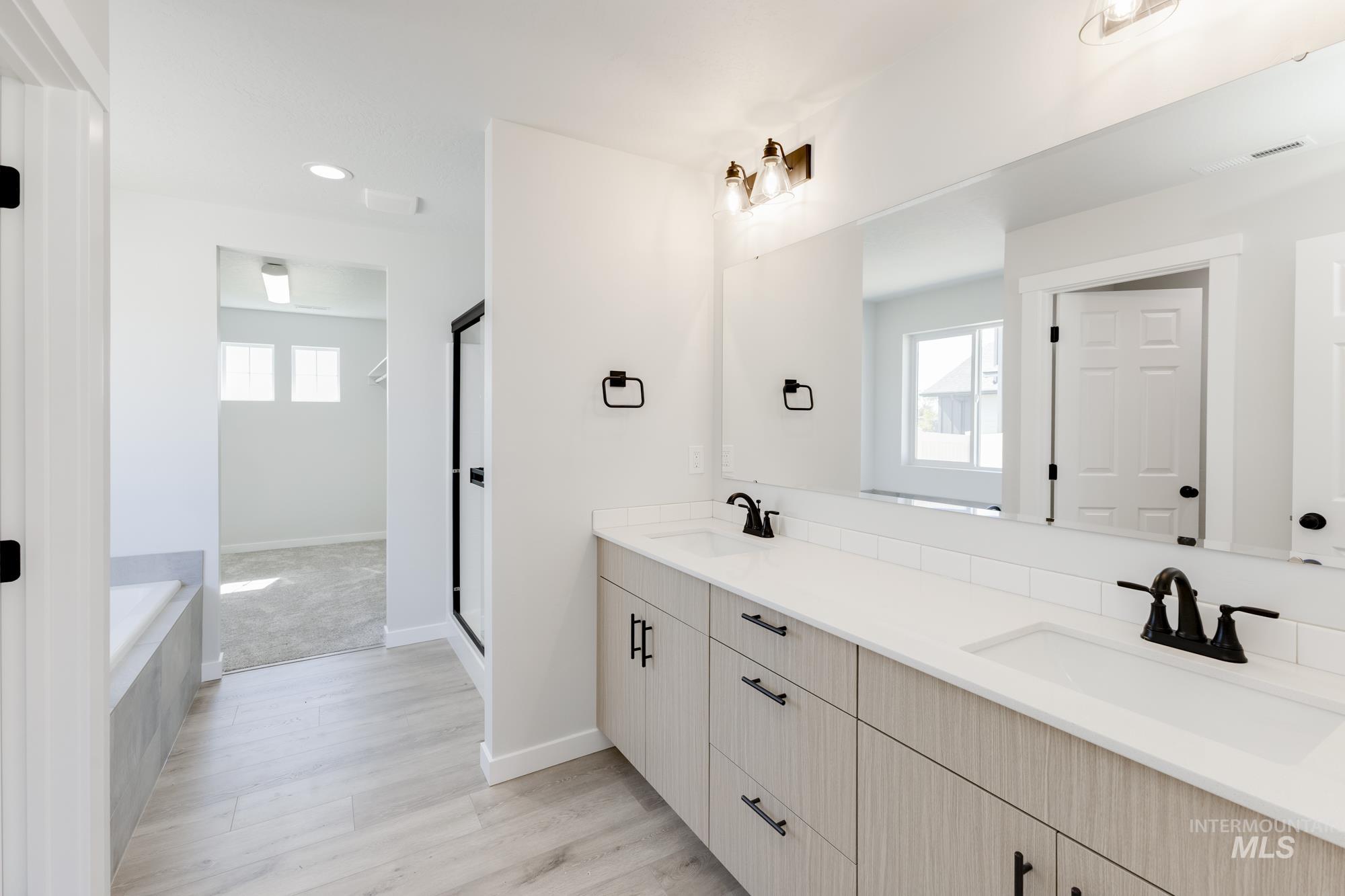 Full bathroom featuring double vanity, a garden tub, recessed lighting, light wood-type flooring, and a stall shower