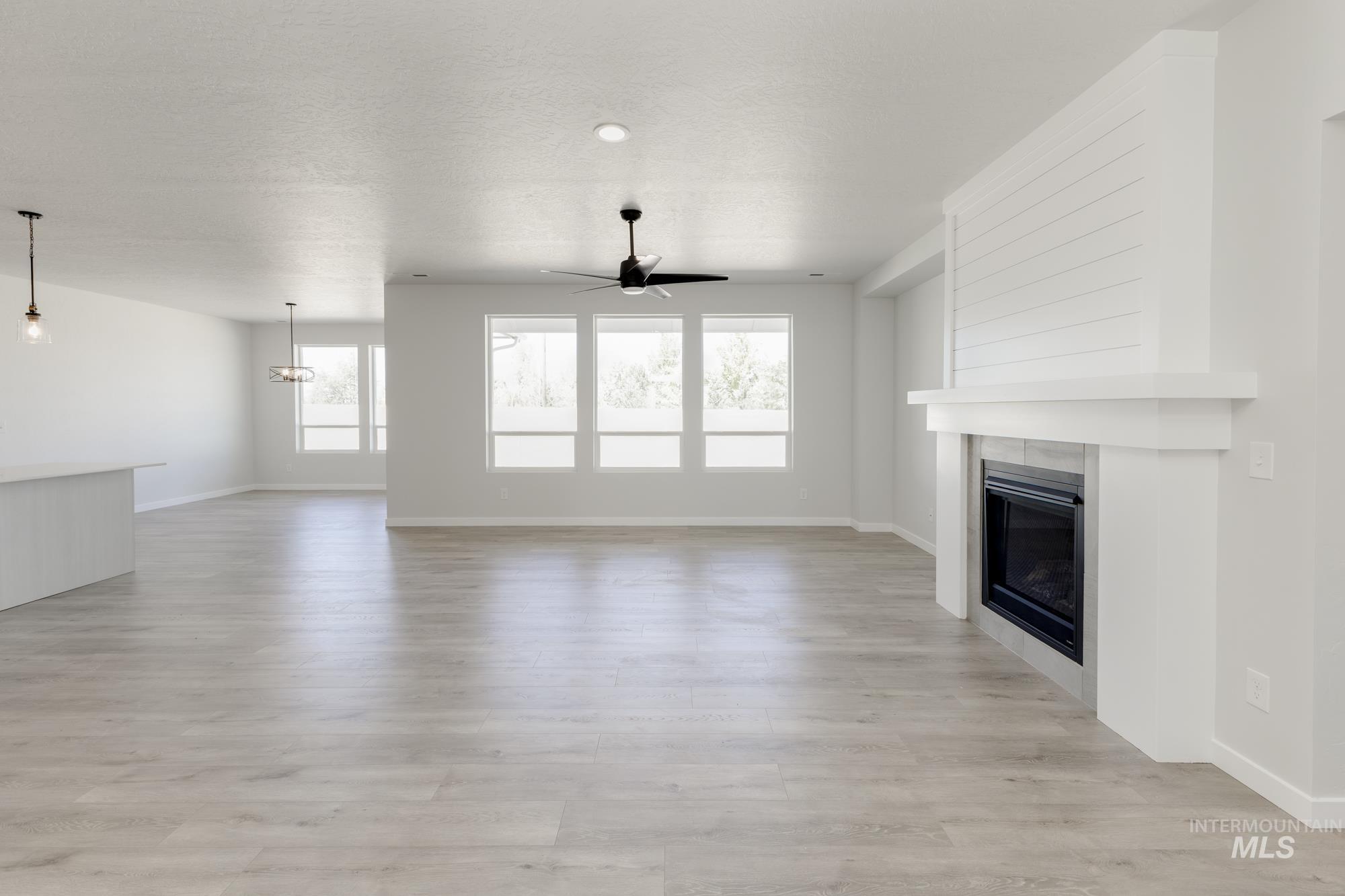 Unfurnished living room with a glass covered fireplace, ceiling fan, light wood-style floors, and a textured ceiling