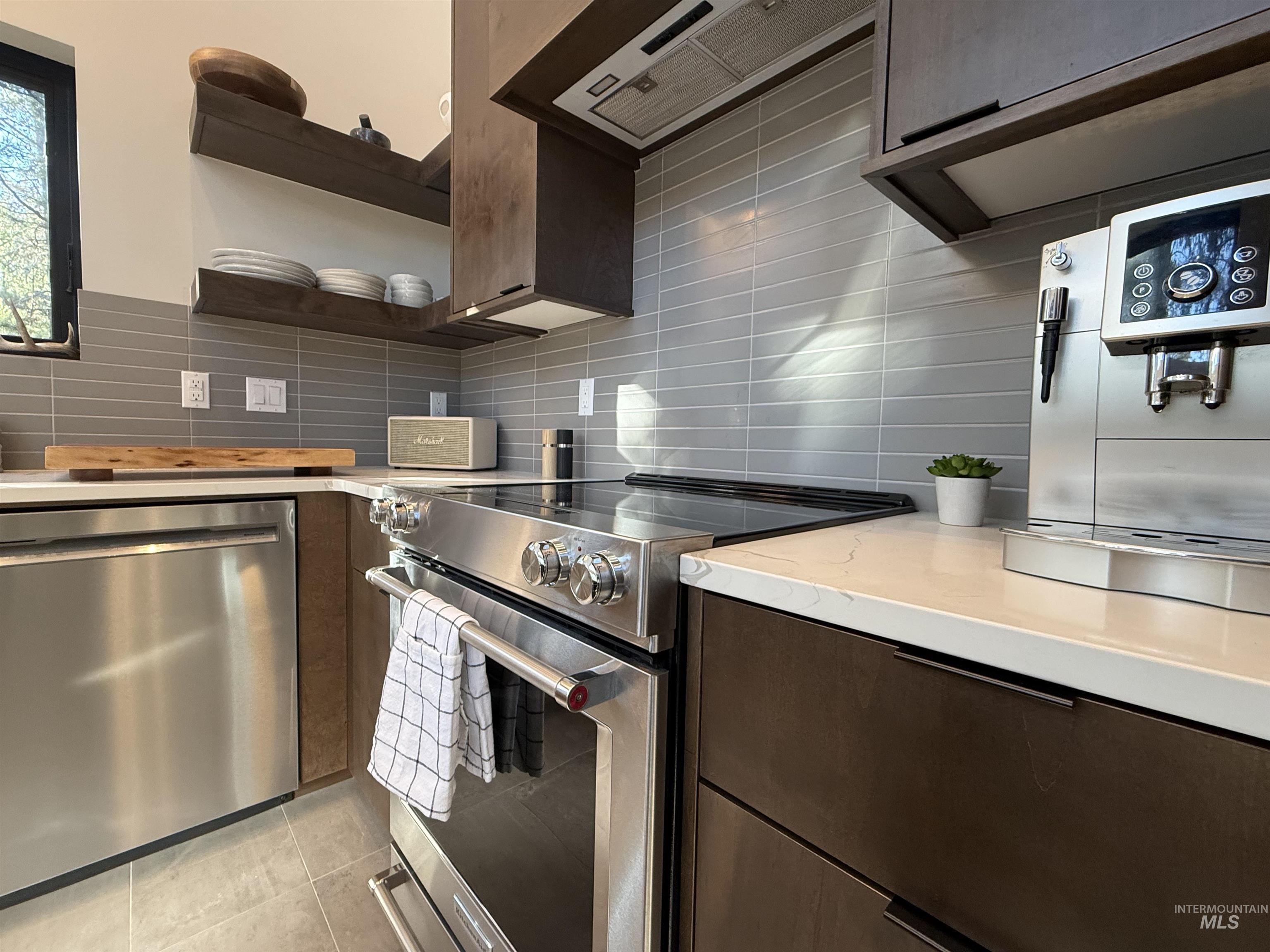 Kitchen with stainless steel appliances, dark wood finish cabinetry, tasteful backsplash, open shelves, and light tile patterned floors