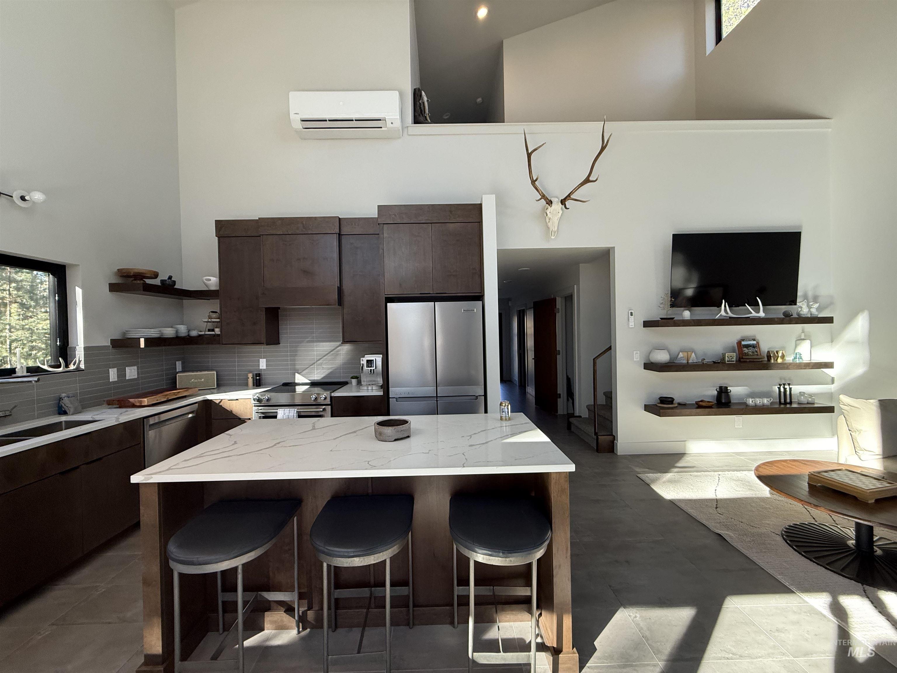 Kitchen with dark wood finish cabinets, stainless steel appliances, a kitchen bar, light stone countertops, and a high ceiling