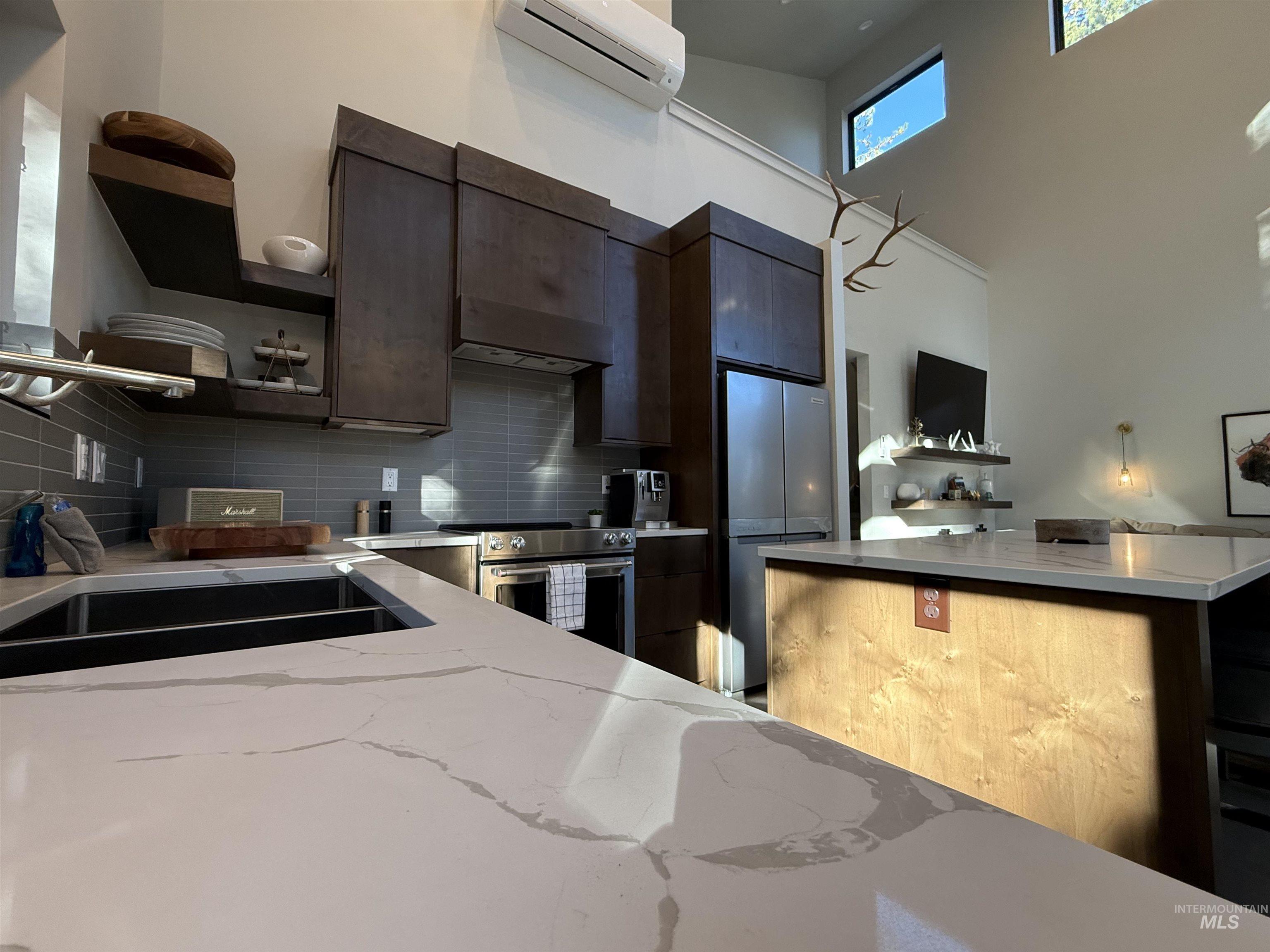 Kitchen with dark wood finish cabinets, a high ceiling, light stone counters, stainless steel appliances, and extractor fan
