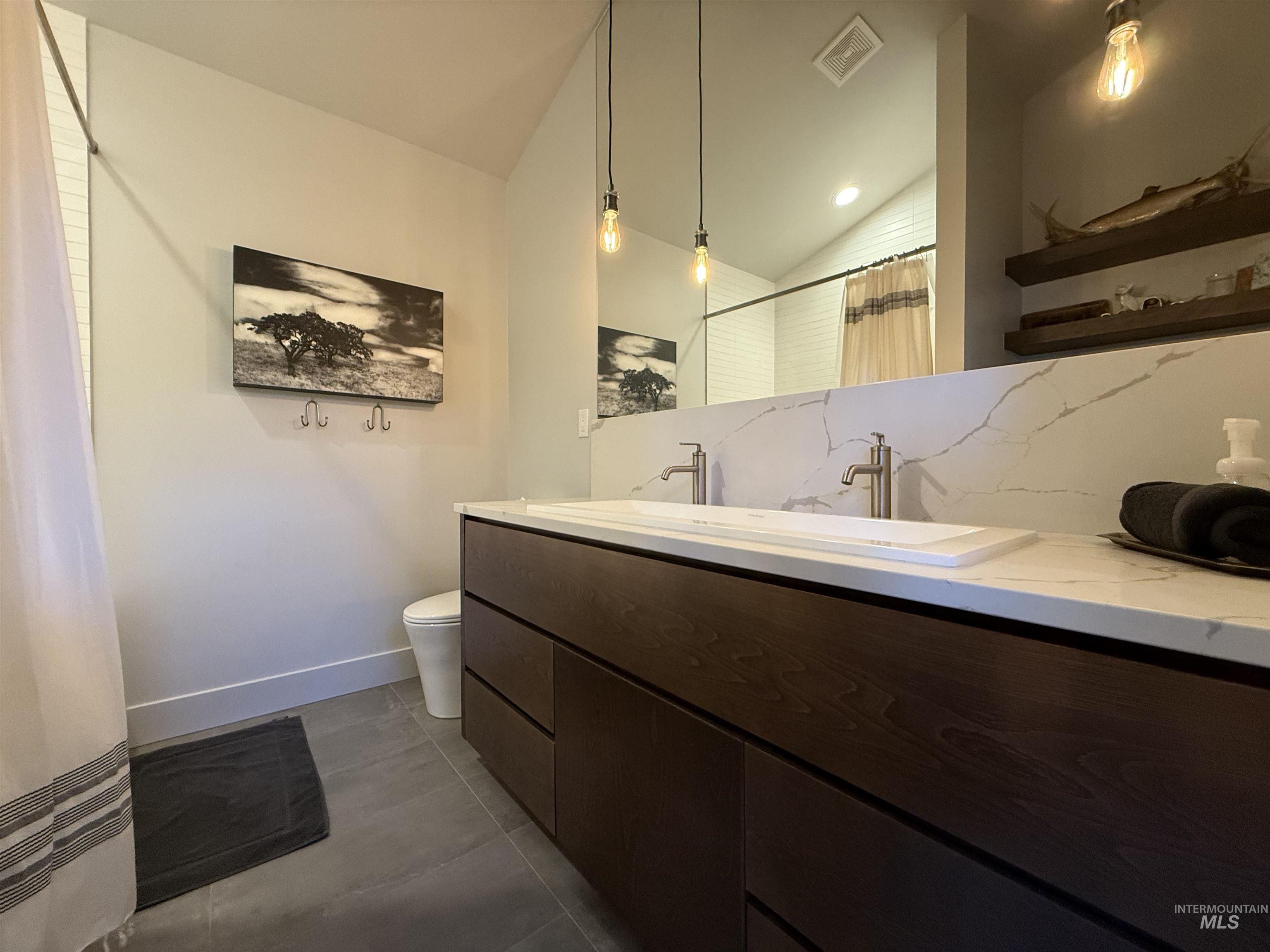 Bathroom with tasteful backsplash, curtained shower, double vanity, lofted ceiling, and dark tile patterned flooring