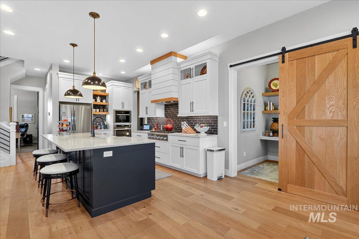 Kitchen with open shelves, a kitchen island with sink, a breakfast bar, hanging light fixtures, and white cabinets
