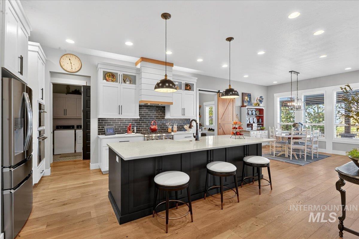 Kitchen with glass insert cabinets, stainless steel appliances, decorative backsplash, dark cabinets, and decorative light fixtures