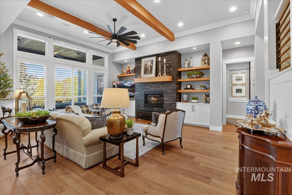 Living room featuring beamed ceiling, light wood-type flooring, a stone fireplace, ceiling fan, and recessed lighting