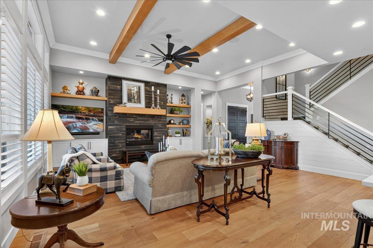 Living area with beam ceiling, light wood-style flooring, stairway, a glass covered fireplace, and ornamental molding