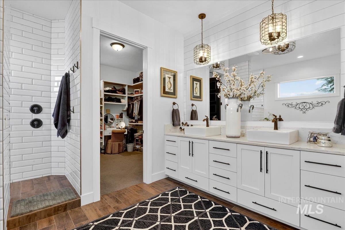 Full bathroom featuring dark wood finished floors, double vanity, a spacious closet, and tiled shower