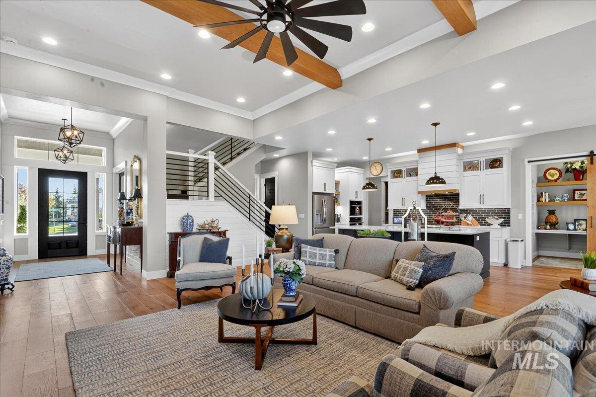 Living room featuring beam ceiling, light wood-style flooring, stairs, crown molding, and recessed lighting