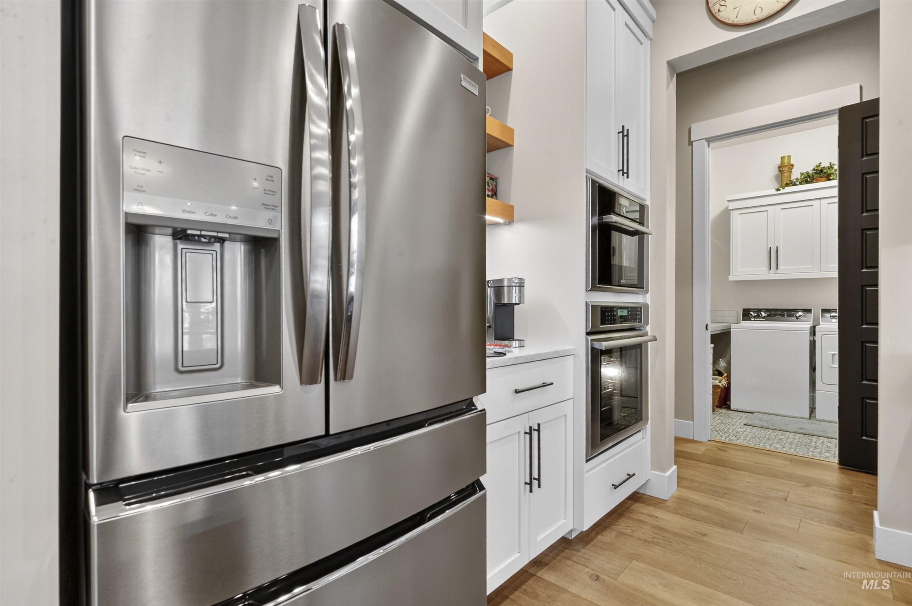 Kitchen with white cabinetry, stainless steel fridge, open shelves, light wood-style floors, and washer and dryer