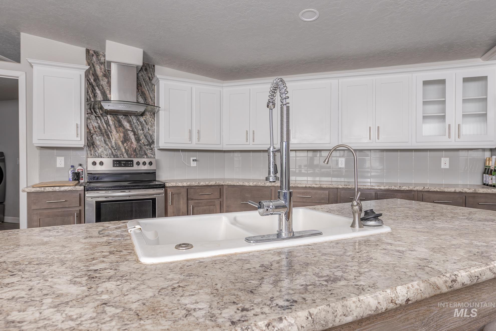 Kitchen with electric stove, decorative backsplash, white cabinetry, wall chimney exhaust hood, and a textured ceiling