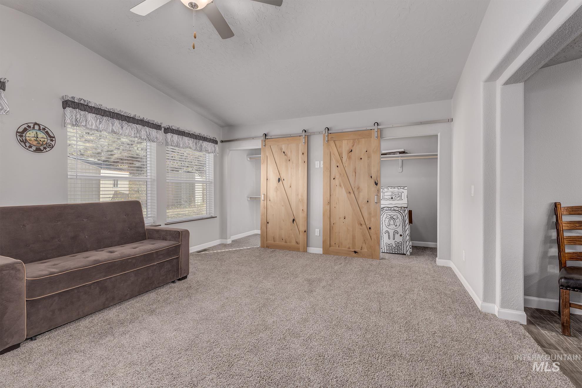 Living area featuring a barn door, carpet floors, vaulted ceiling, and ceiling fan
