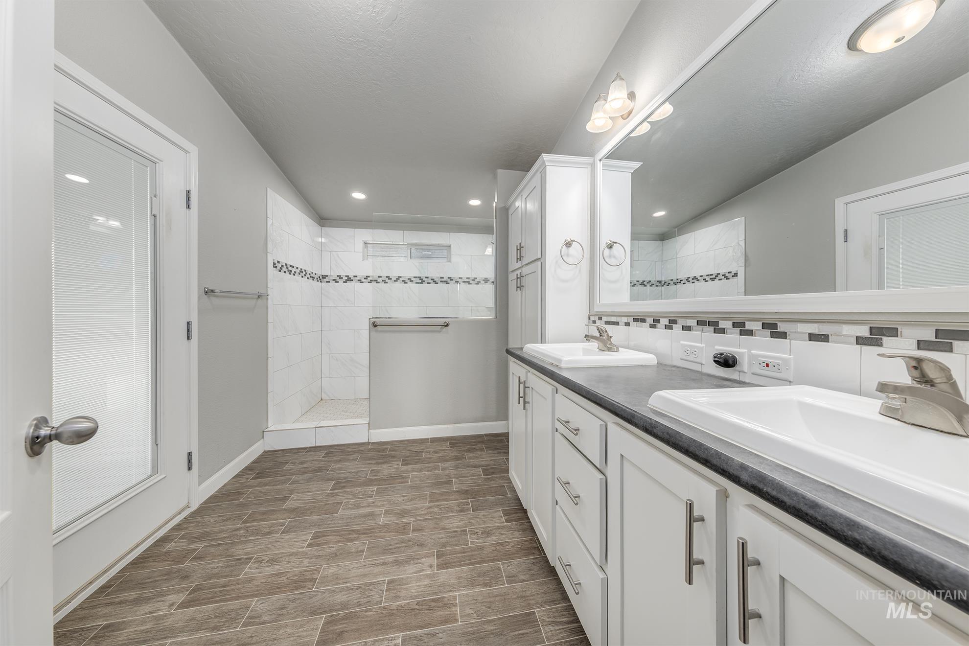 Full bath with a walk in shower, double vanity, recessed lighting, wood tiled floors, and tasteful backsplash