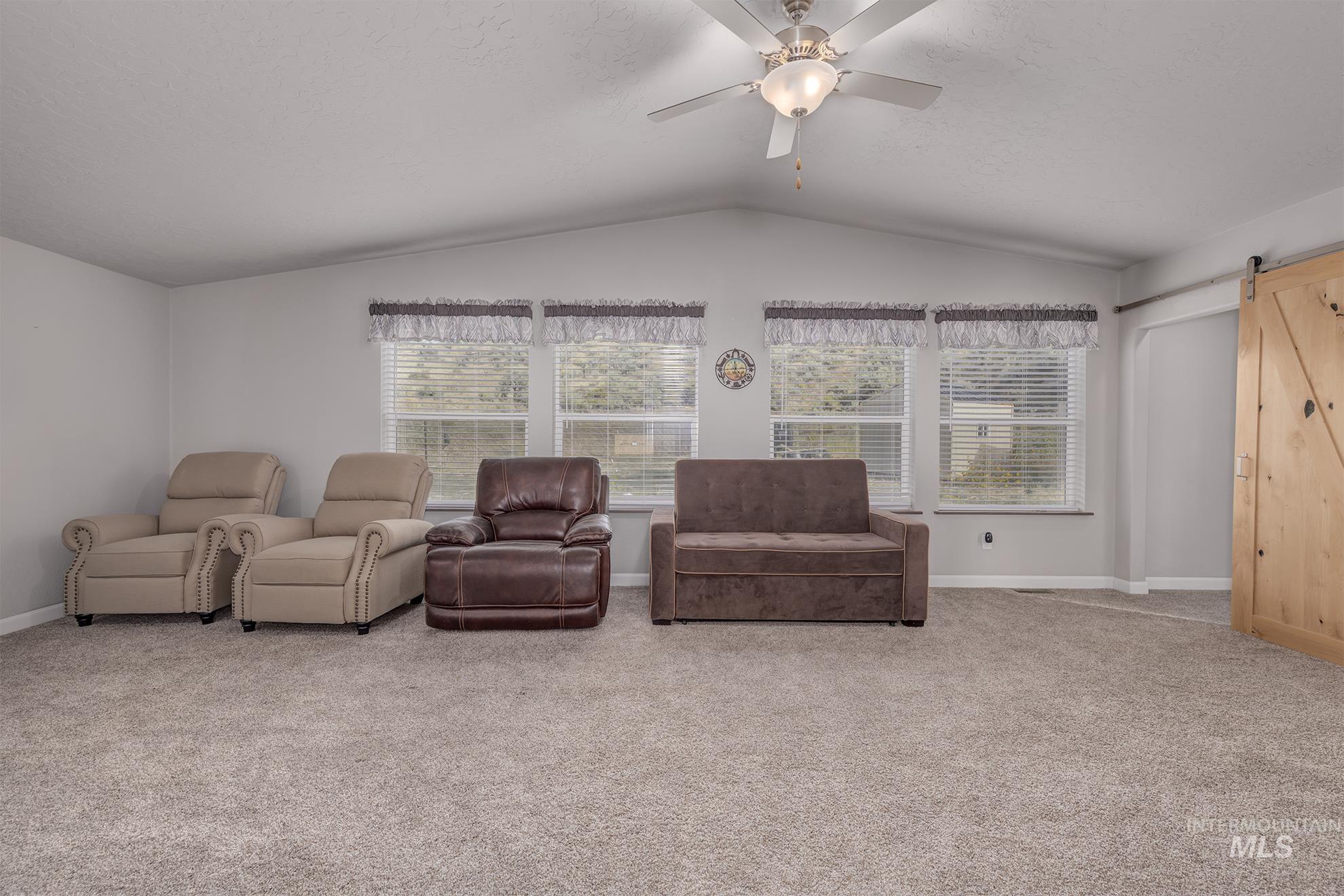 Living room featuring a barn door, carpet floors, lofted ceiling, and a ceiling fan