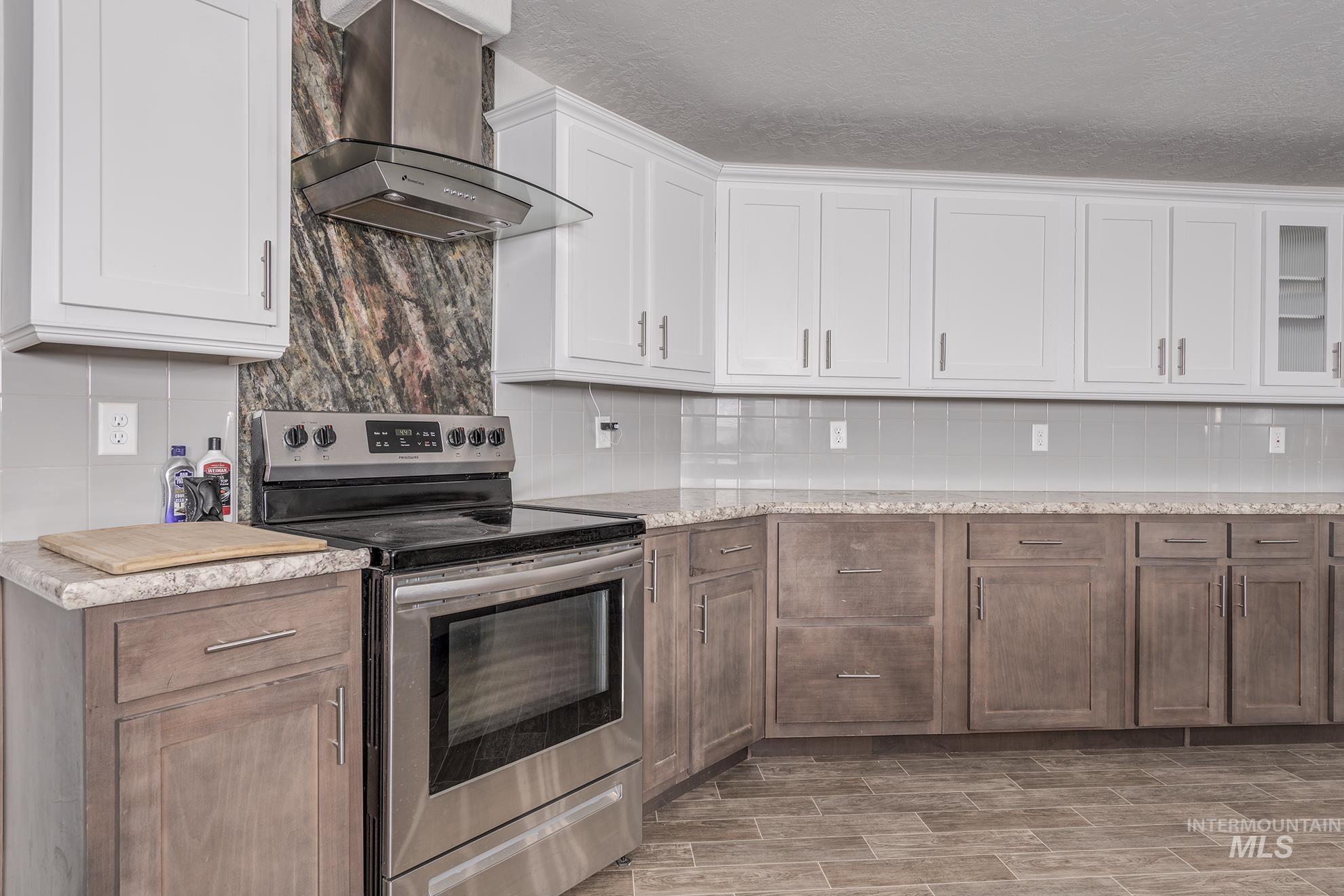 Kitchen featuring electric range, wall chimney exhaust hood, backsplash, white cabinetry, and wood tiled floors