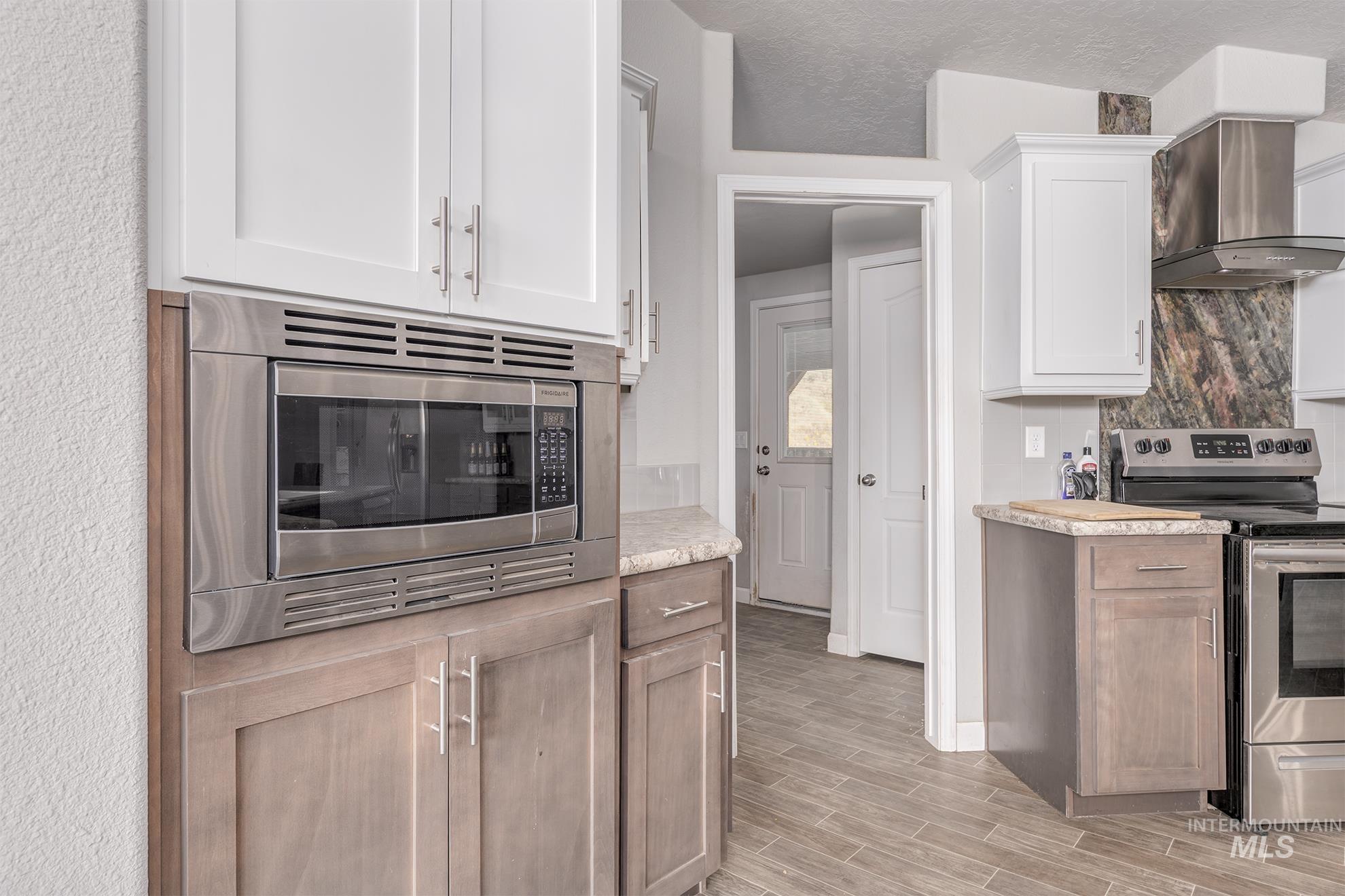 Kitchen featuring stainless steel appliances, wall chimney range hood, wood finish floors, white cabinets, and tasteful backsplash