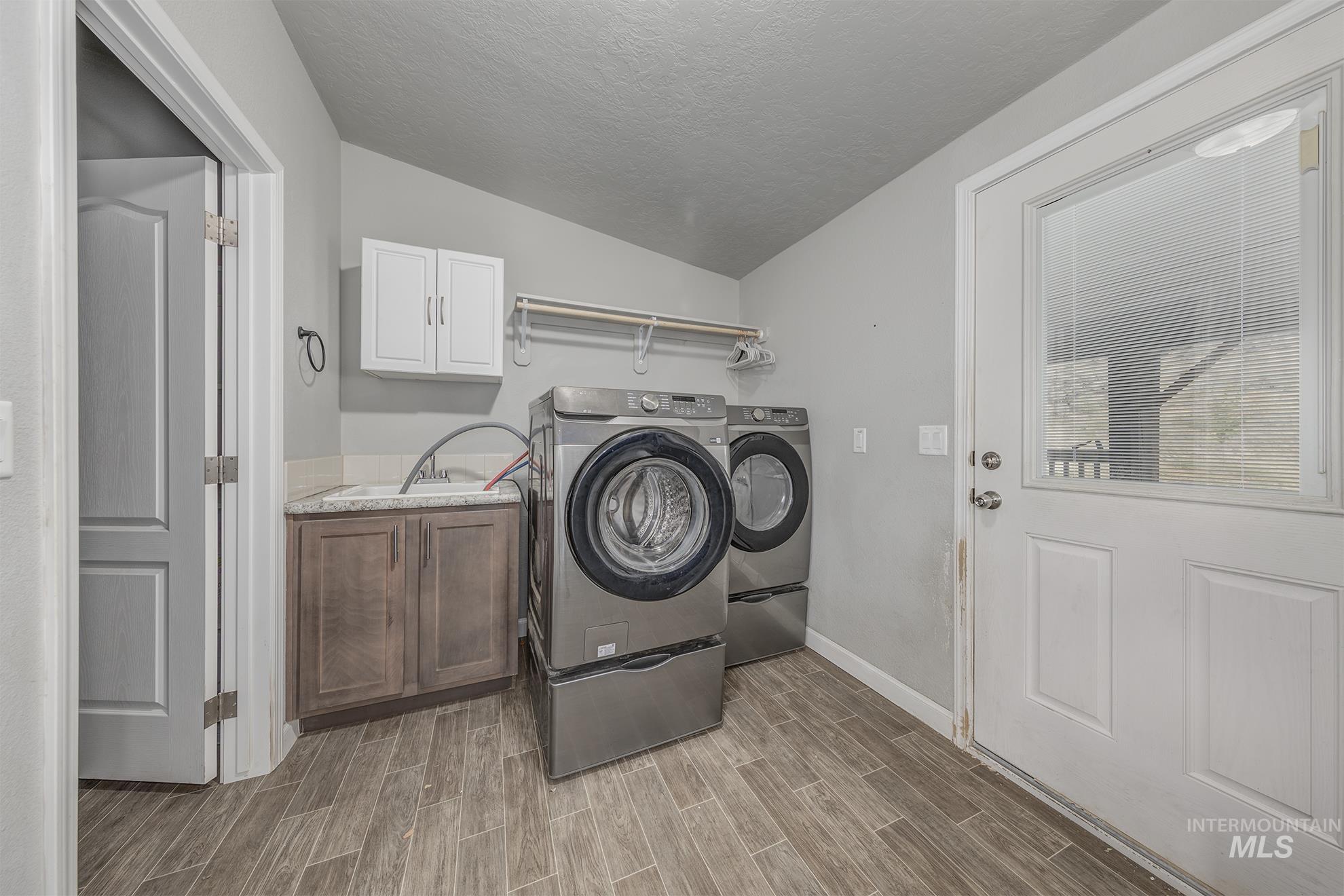 Laundry room with a textured ceiling, wood tiled floors, cabinet space, and washing machine and dryer