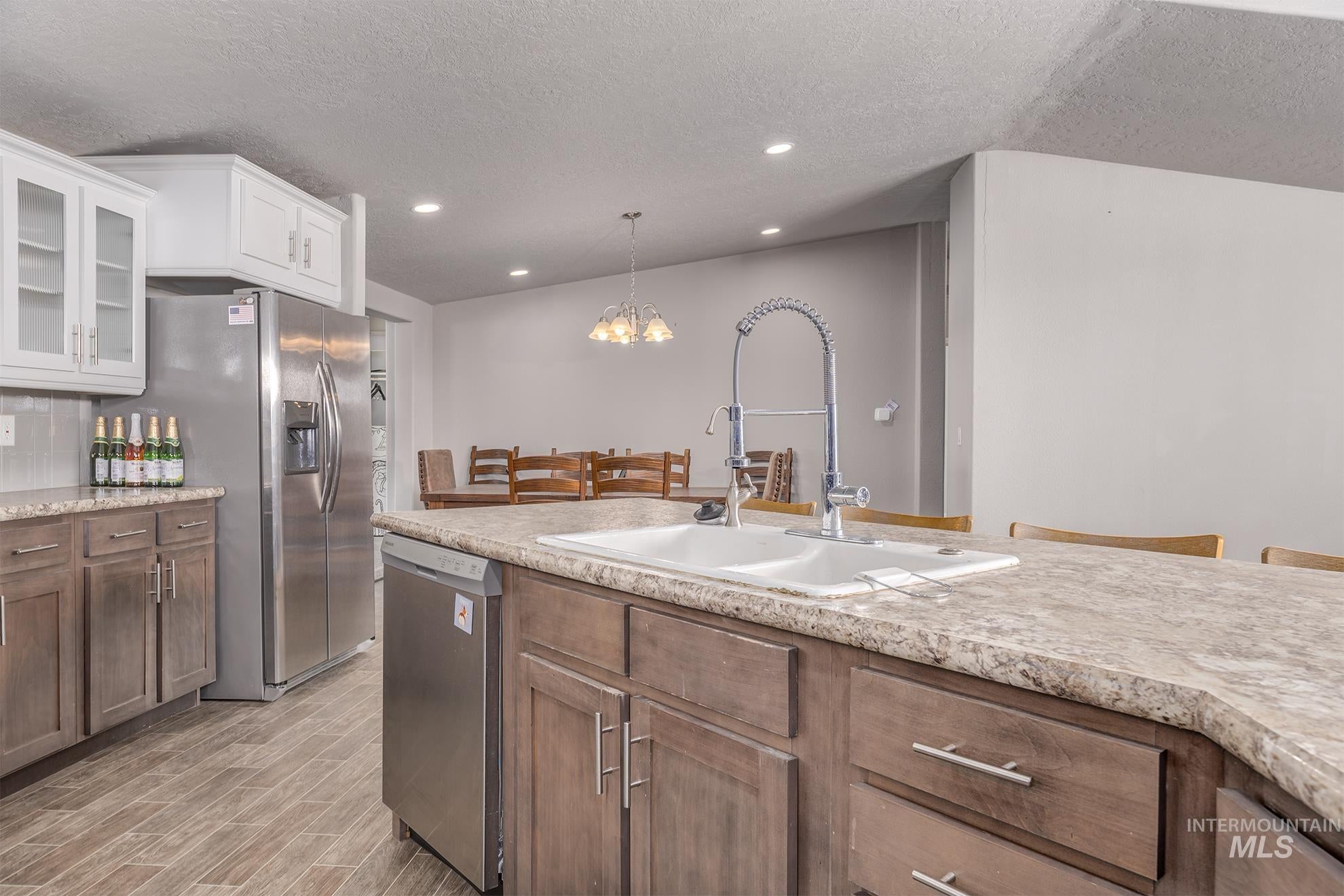 Kitchen with a chandelier, glass insert cabinets, appliances with stainless steel finishes, a textured ceiling, and decorative light fixtures