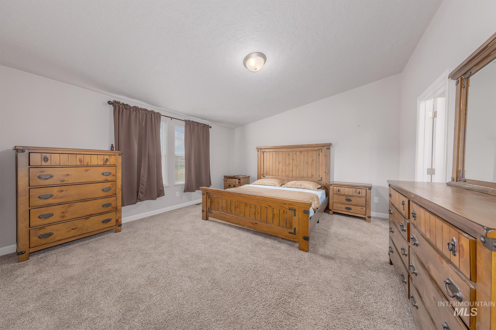 Bedroom with lofted ceiling, light colored carpet, and a textured ceiling