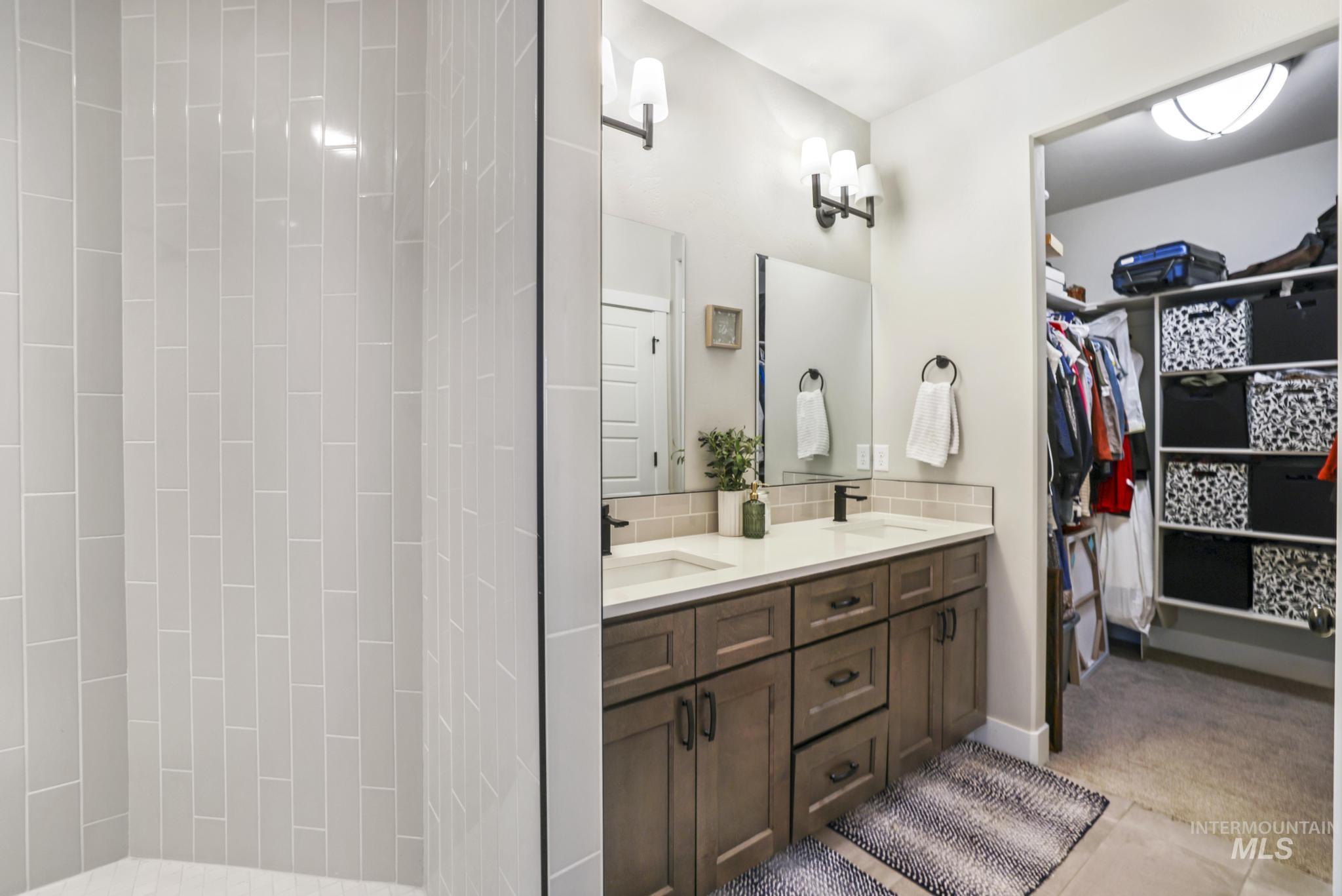 Bathroom featuring double vanity, a spacious closet, curtained shower, and backsplash