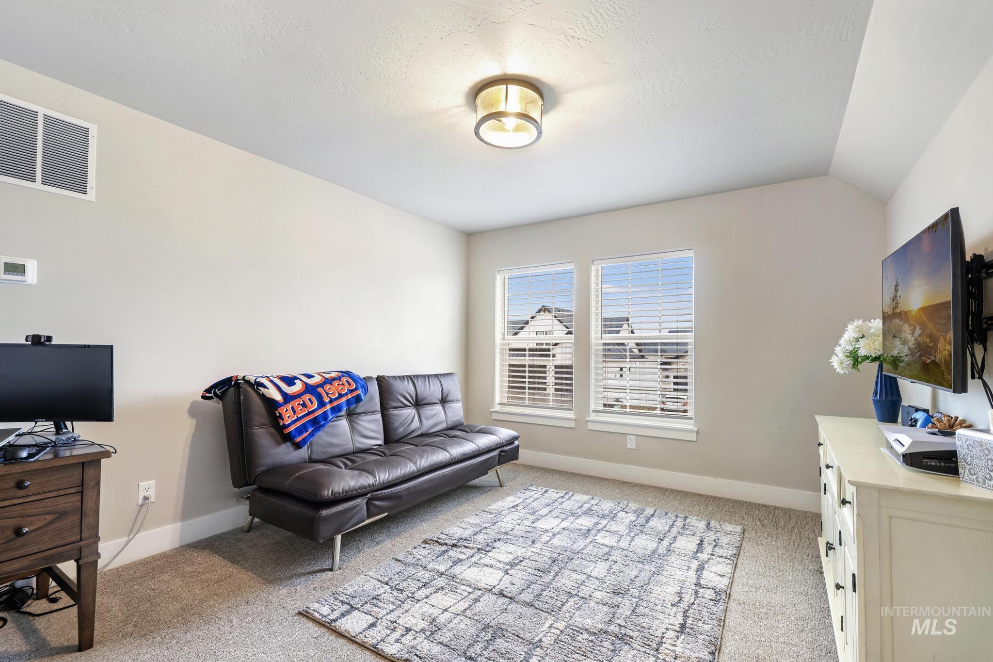 Living area with light carpet, vaulted ceiling, and a desk