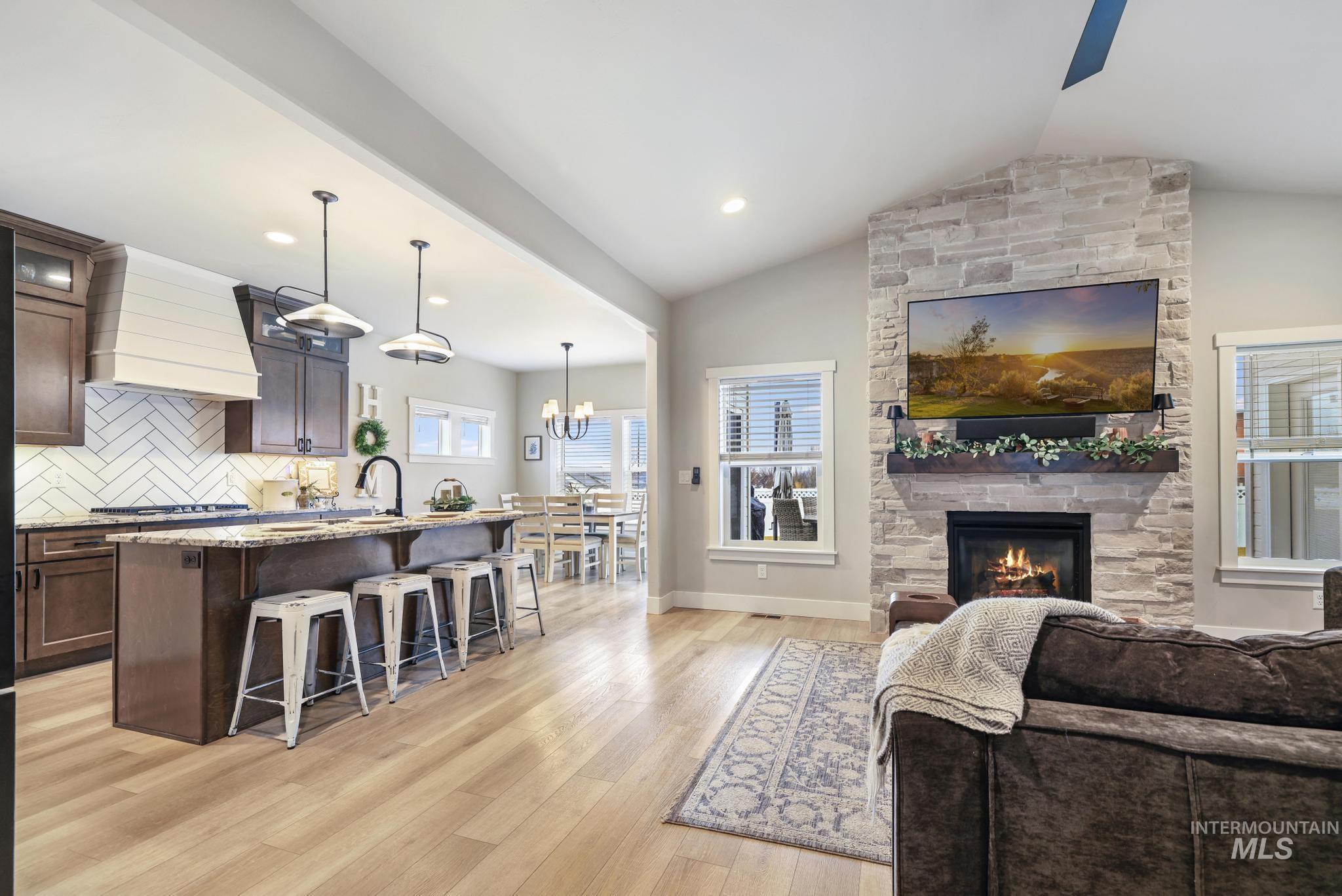 Living area featuring a fireplace, lofted ceiling, light wood-style floors, a ceiling fan, and a chandelier
