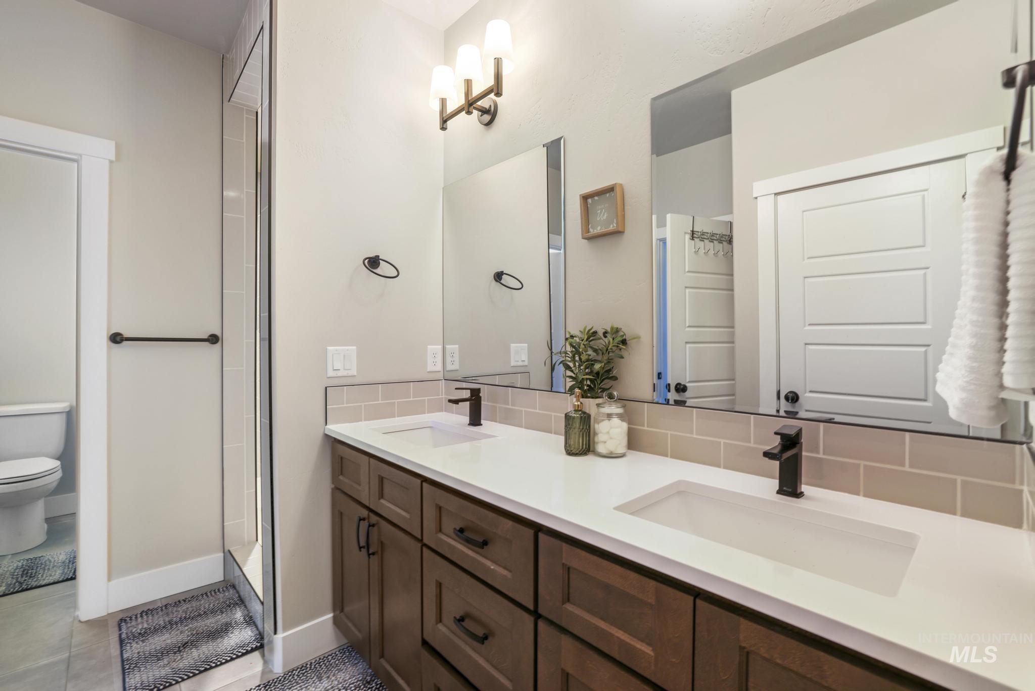 Bathroom with double vanity, walk in shower, and decorative backsplash