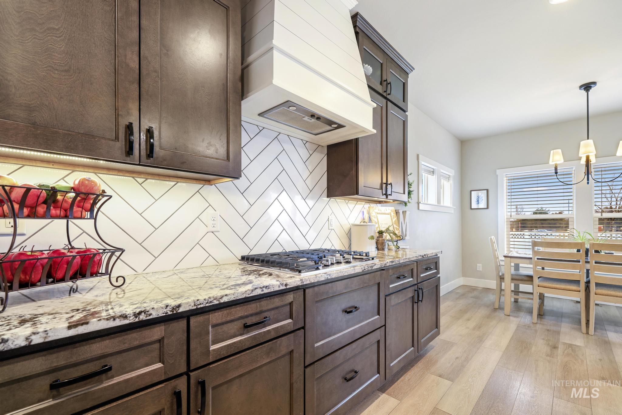 Kitchen with light stone counters, dark wood finish cabinetry, light wood-style floors, backsplash, and stainless steel gas stovetop