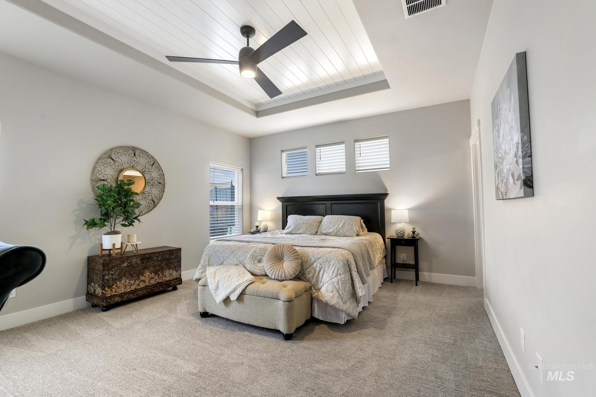 Bedroom featuring carpet, a wooden tray ceiling, and a ceiling fan